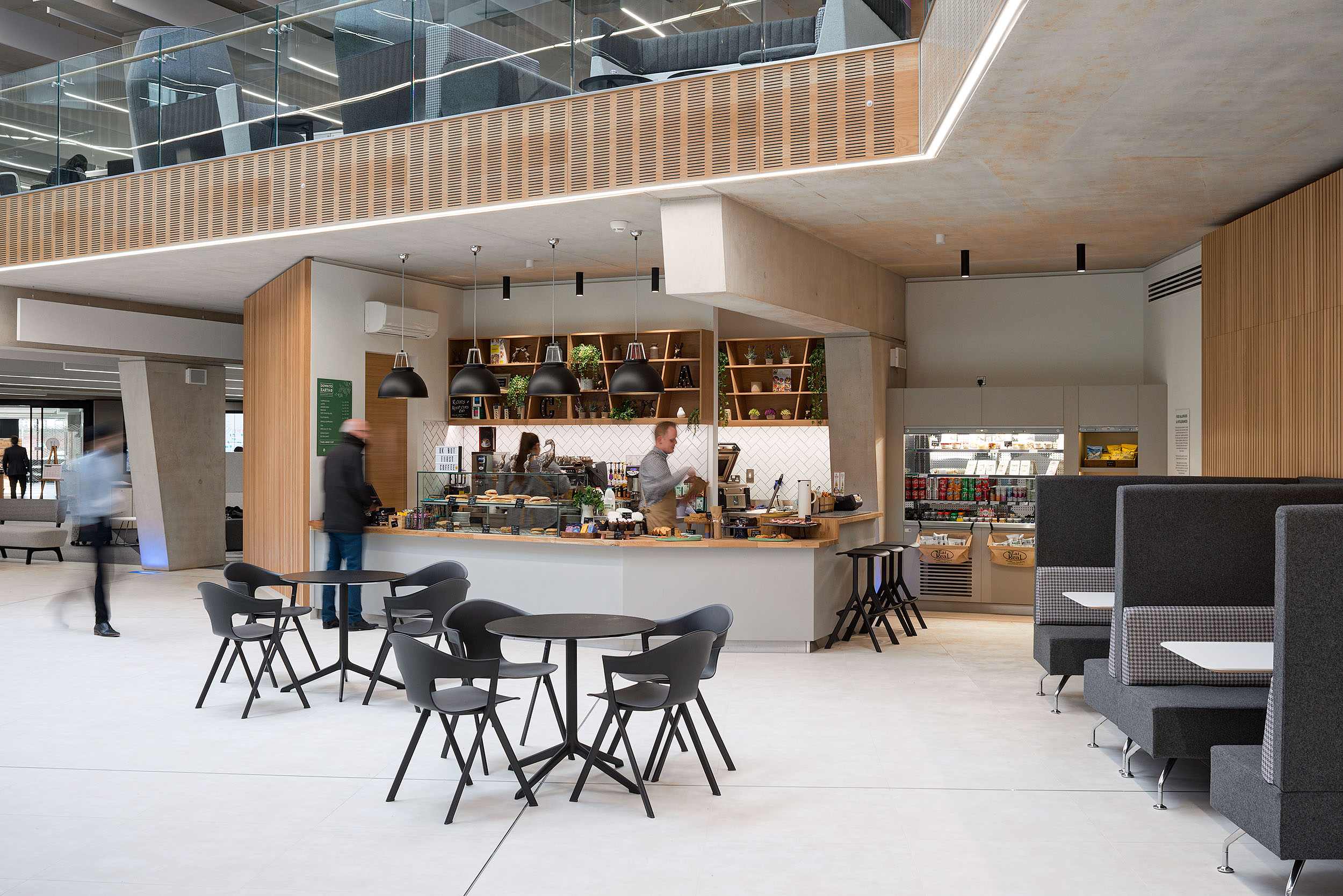 A café at Atkins Woodcote Grove, with a variety of seating options including booth seating and small round tables, alongside a coffee counter.