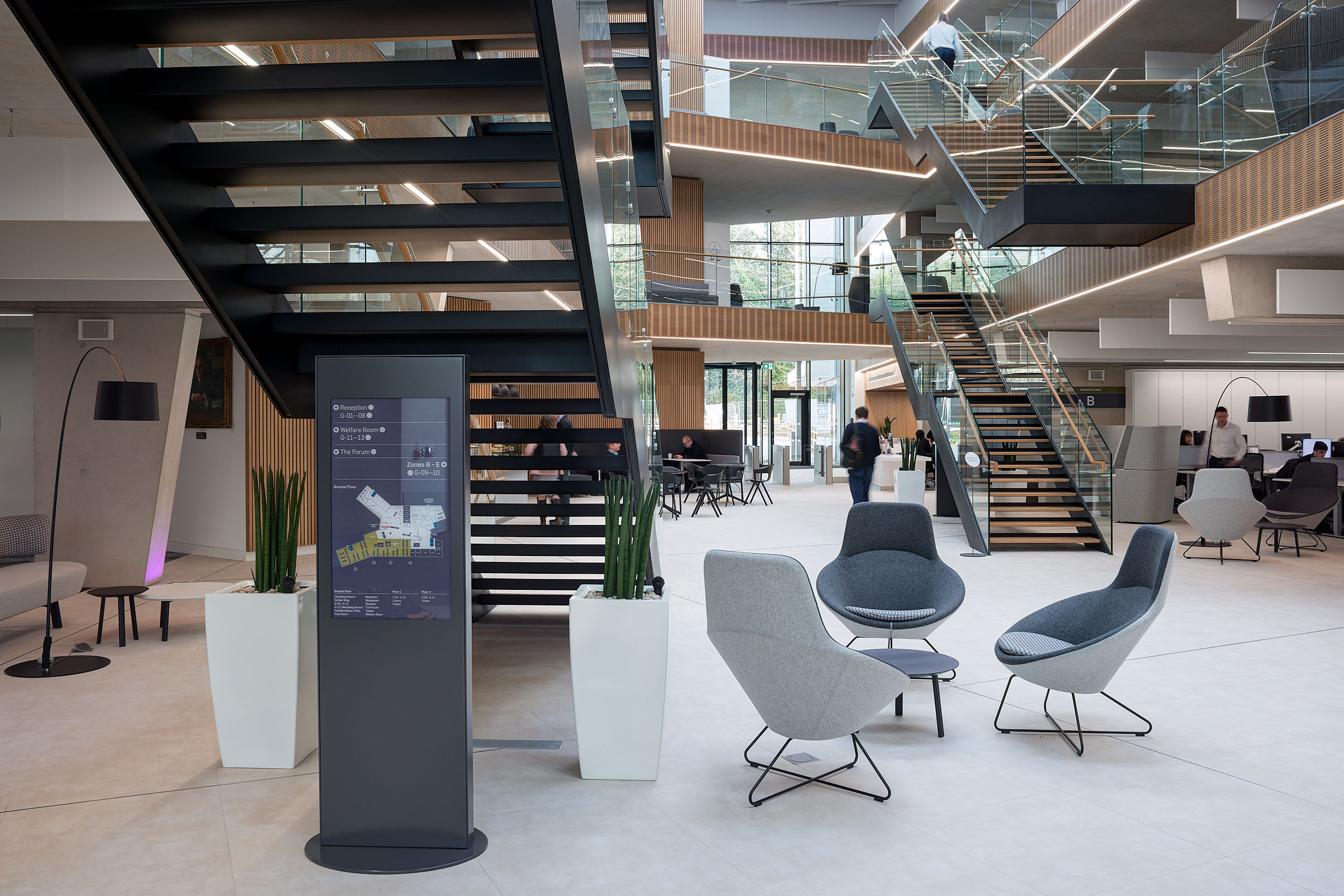 Seating area under a staircase in the open atrium at Atkins Woodcote Grove, with comfortable chairs and modern furniture.