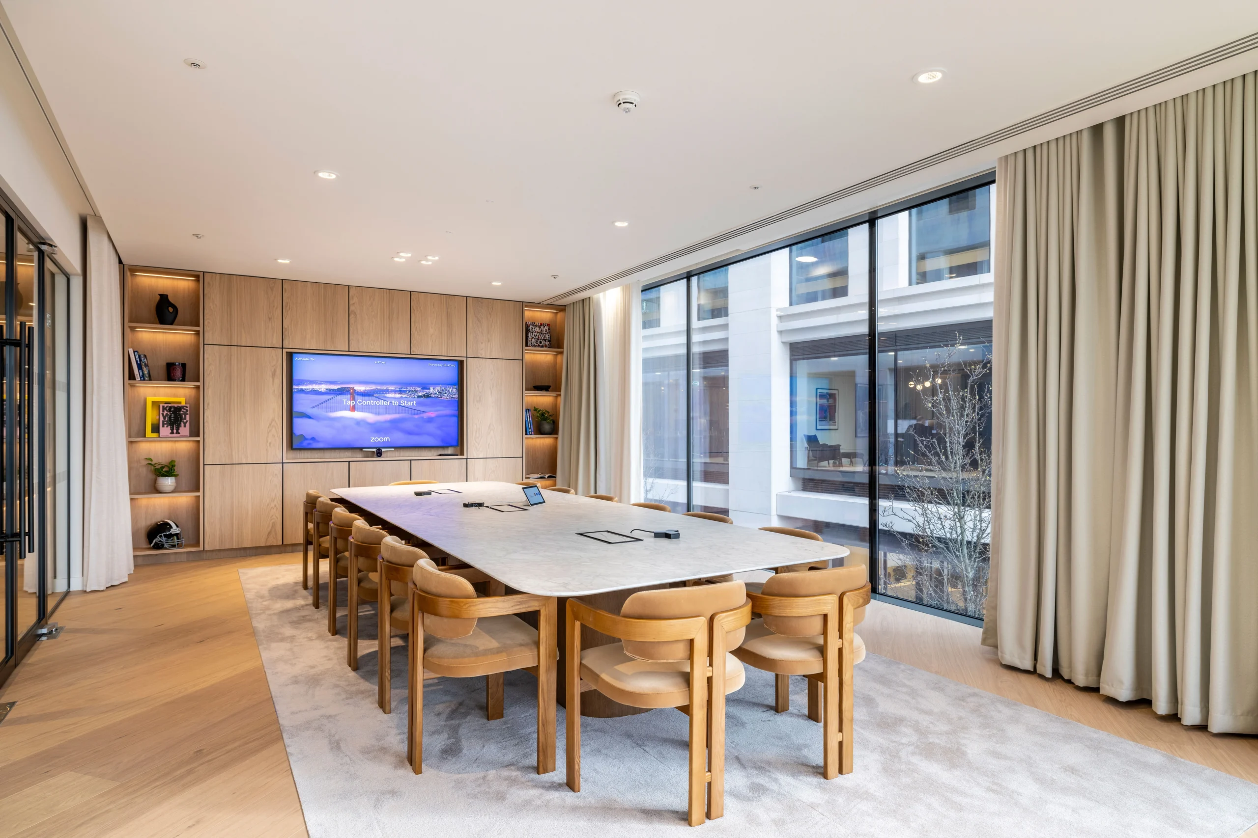 A meeting room at Authentic Brand Group, designed by Modus, with a long conference table, beige chairs, and floor-to-ceiling windows allows natural light to flood the space.