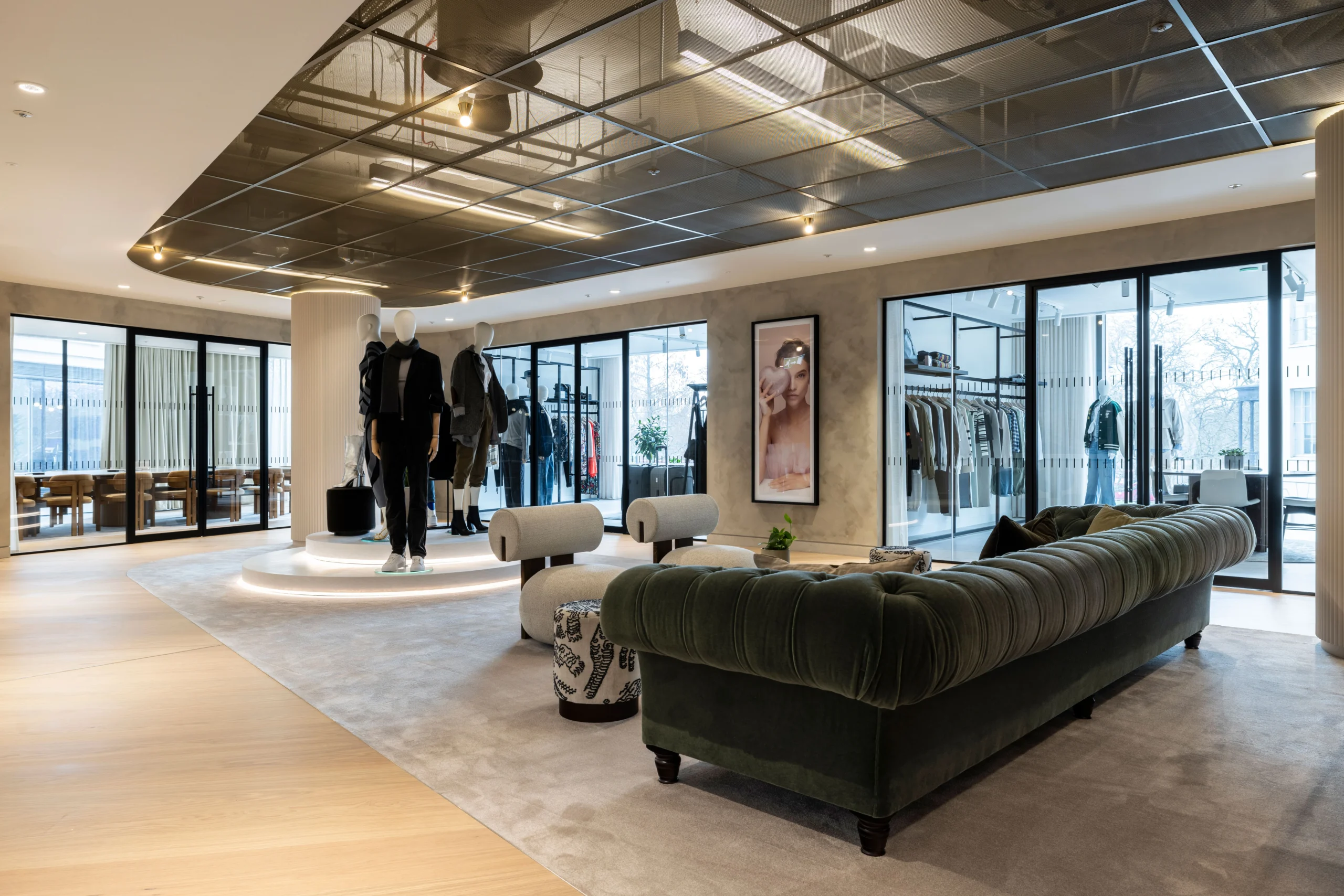 A stylish display area at Authentic Brand Group, designed by Modus, featuring mannequins on a raised platform, velvet green sofas, and glass doors leading to a retail-inspired setting.
