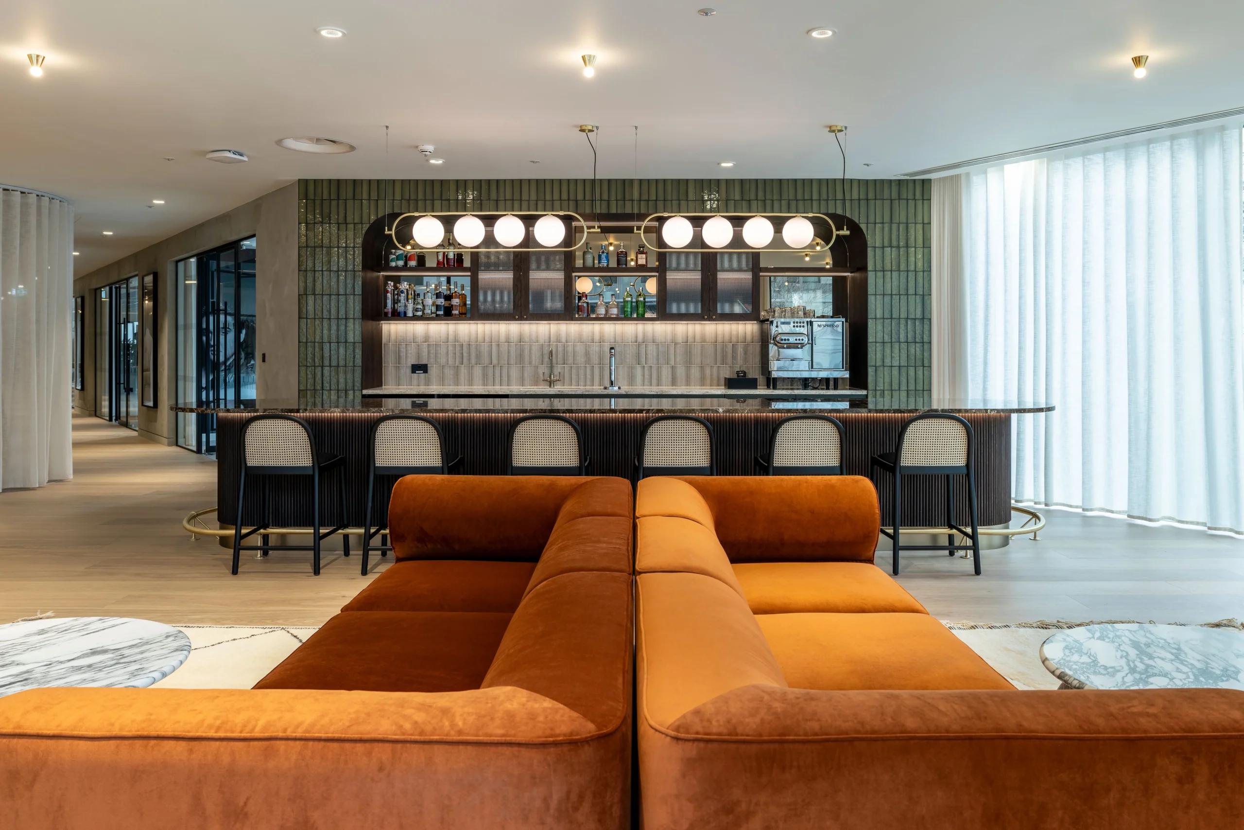 A spacious lounge area at Authentic Brand Group, designed by Modus, with mustard-coloured armchairs, a large ottoman, and open-plan workstations in the background, highlighted by modern lighting and greenery.