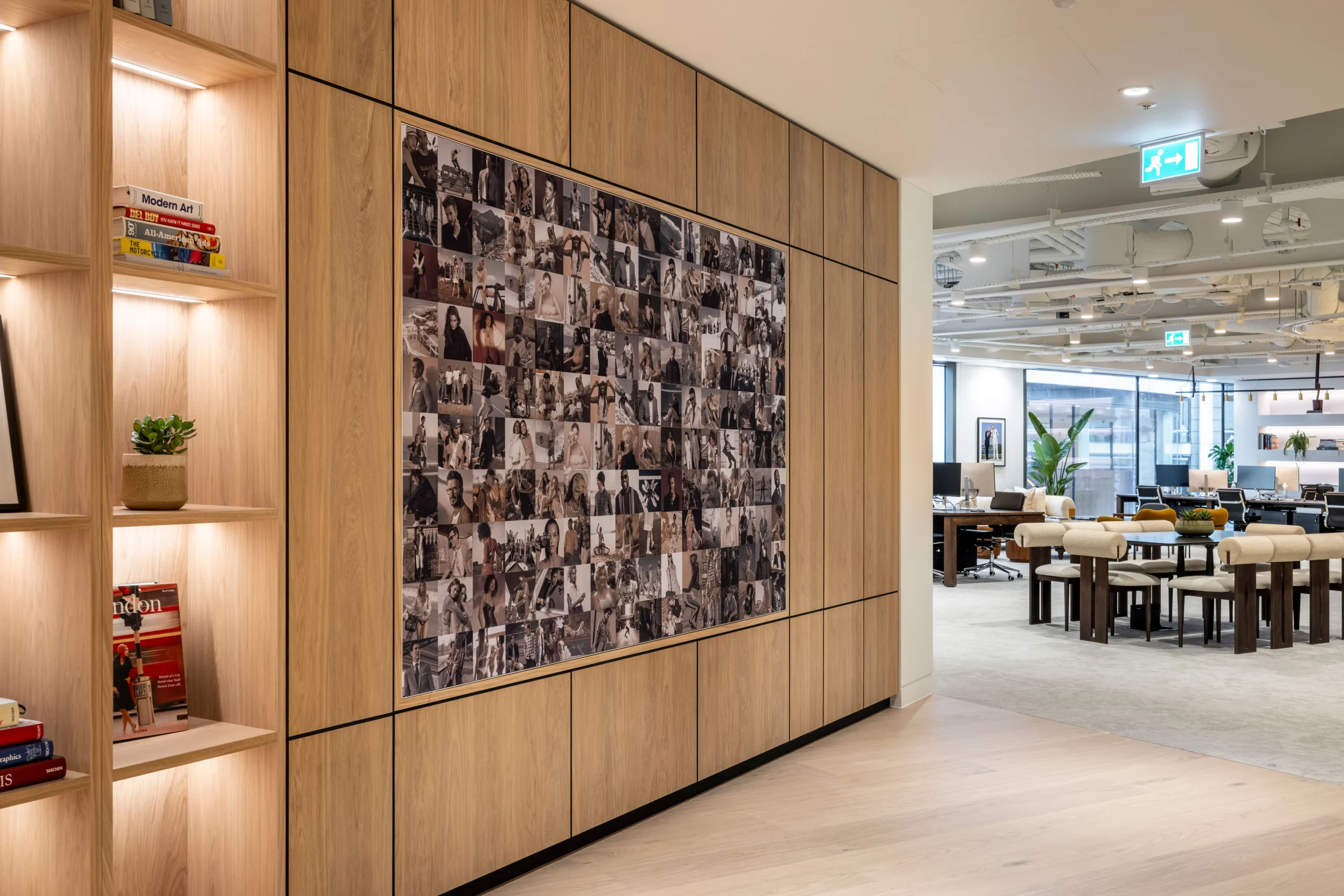 A feature wall at Authentic Brand Group, designed by Modus, displays a collage of black-and-white images of people surrounded by wooden panelling and integrated shelves displaying books and plants.