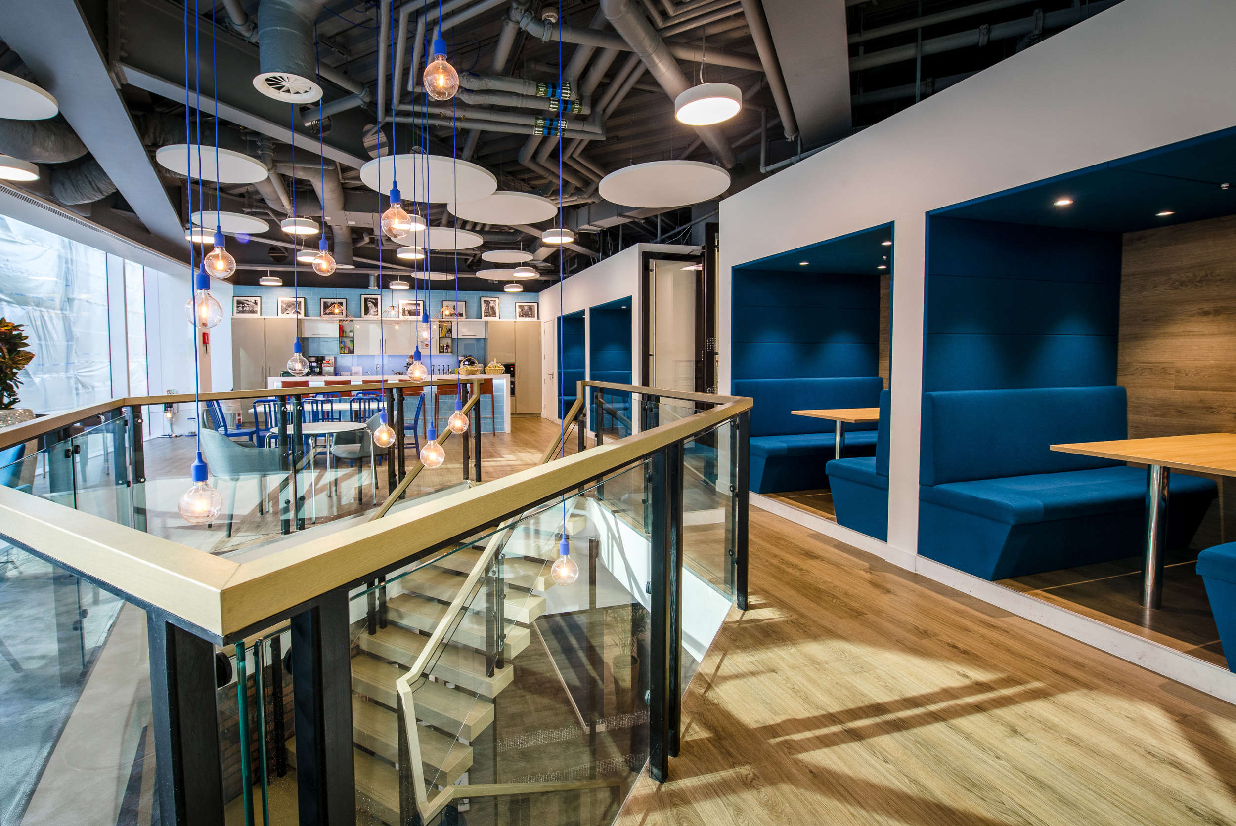 CRA stylish bespoke breakout office space designed by Modus for Charles River Associates, featuring glass railings and blue booth seating.