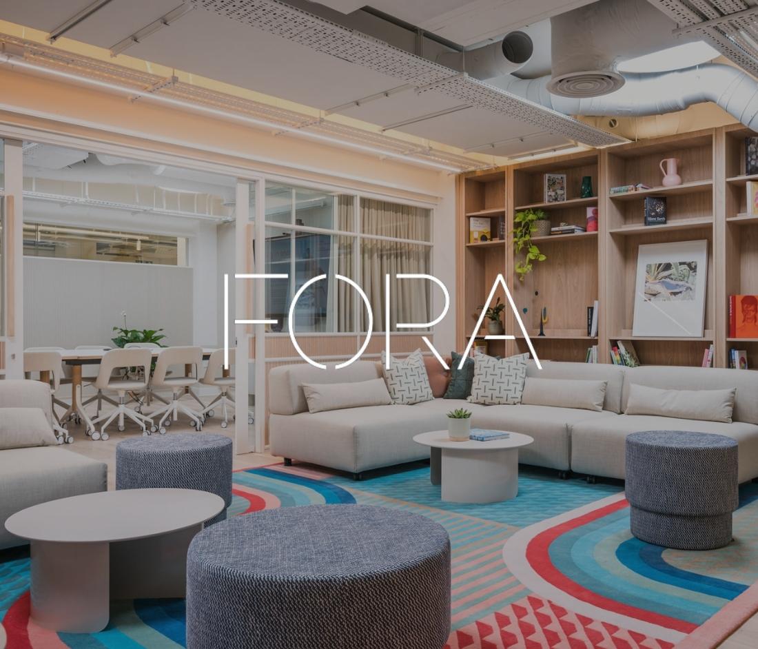 Contemporary lounge space at Fora Wells Mews featuring cozy seating, colorful rugs, and a meeting room in the background.