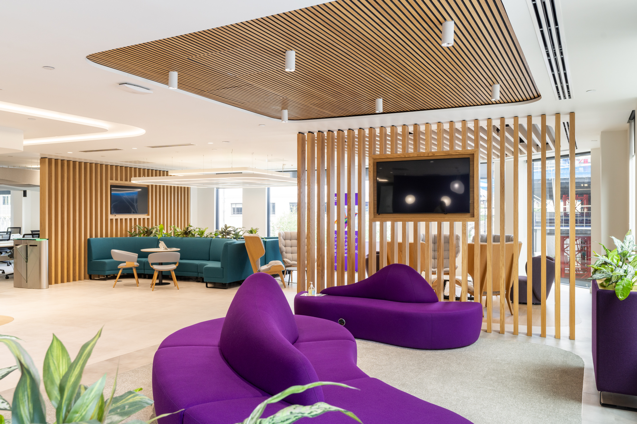 DXC Technology's stylish breakout area with vibrant purple seating, teal sofas, and a wooden slatted divider creates a relaxing atmosphere.