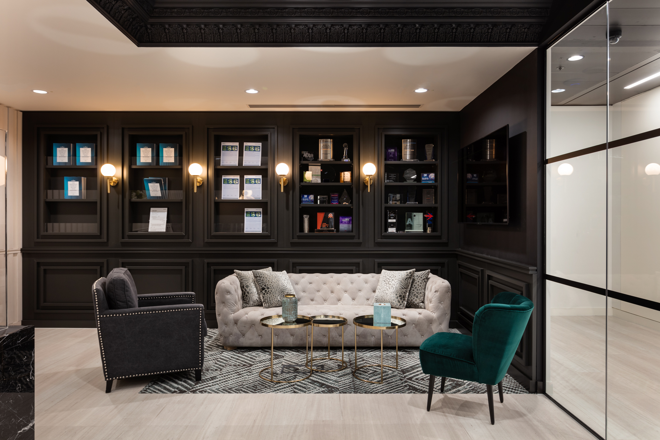Finncap's modern lounge area features a tufted beige sofa, a dark grey armchair, a teal velvet chair, and decorative shelves with awards.