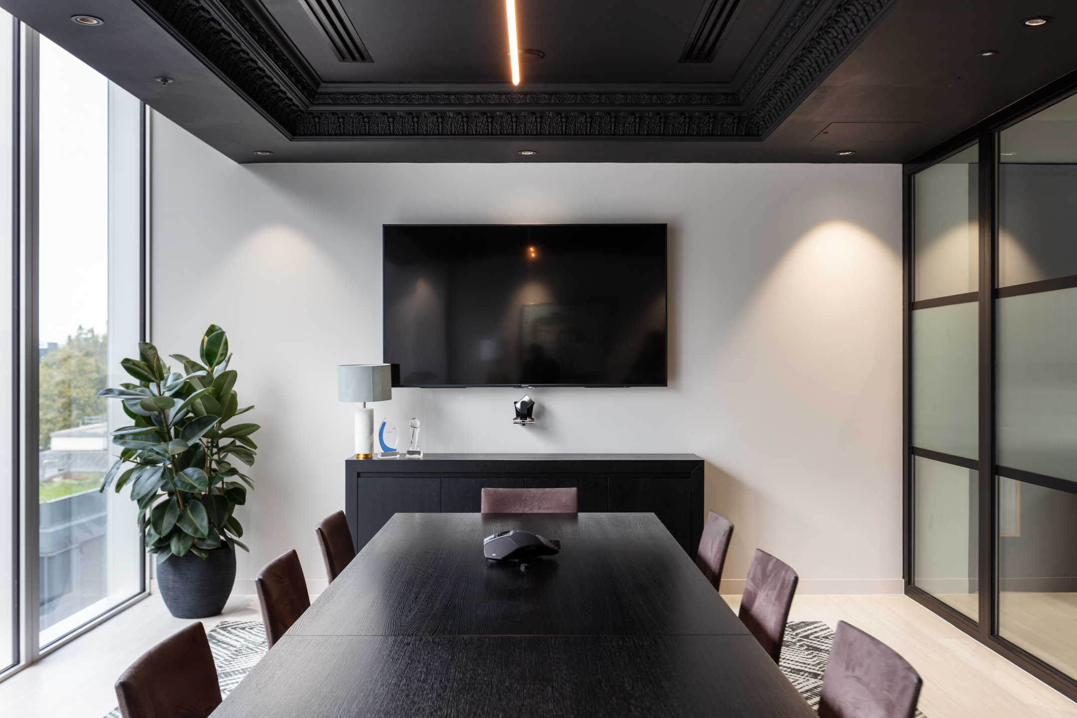 Finncap meeting room showcasing a sleek black conference table, leather chairs, and a large TV screen, with minimalistic decor and natural light from floor-to-ceiling windows.
