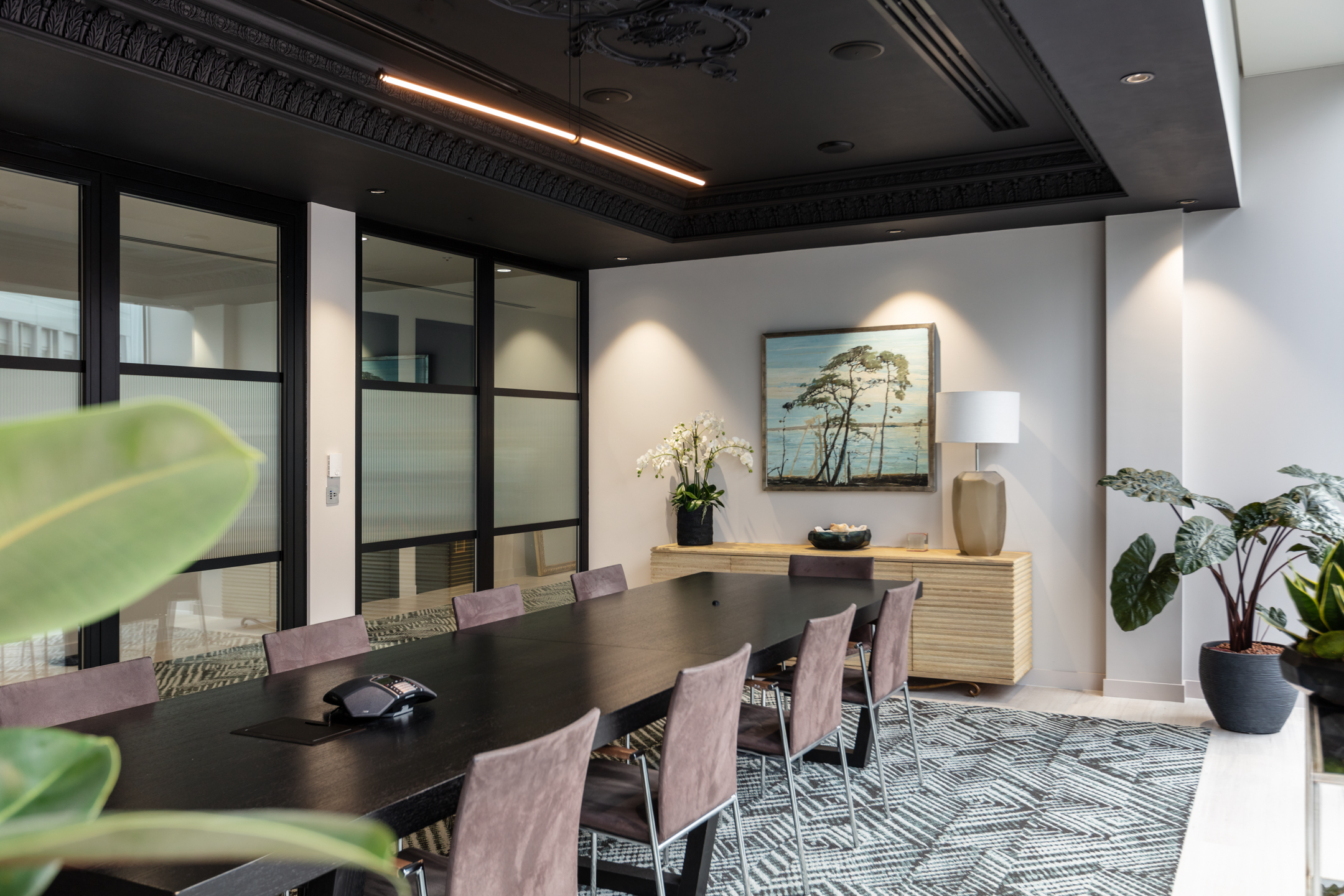 Finncap boardroom with a large black table, brown chairs, plants, a geometrical carpet, and neutral artwork.