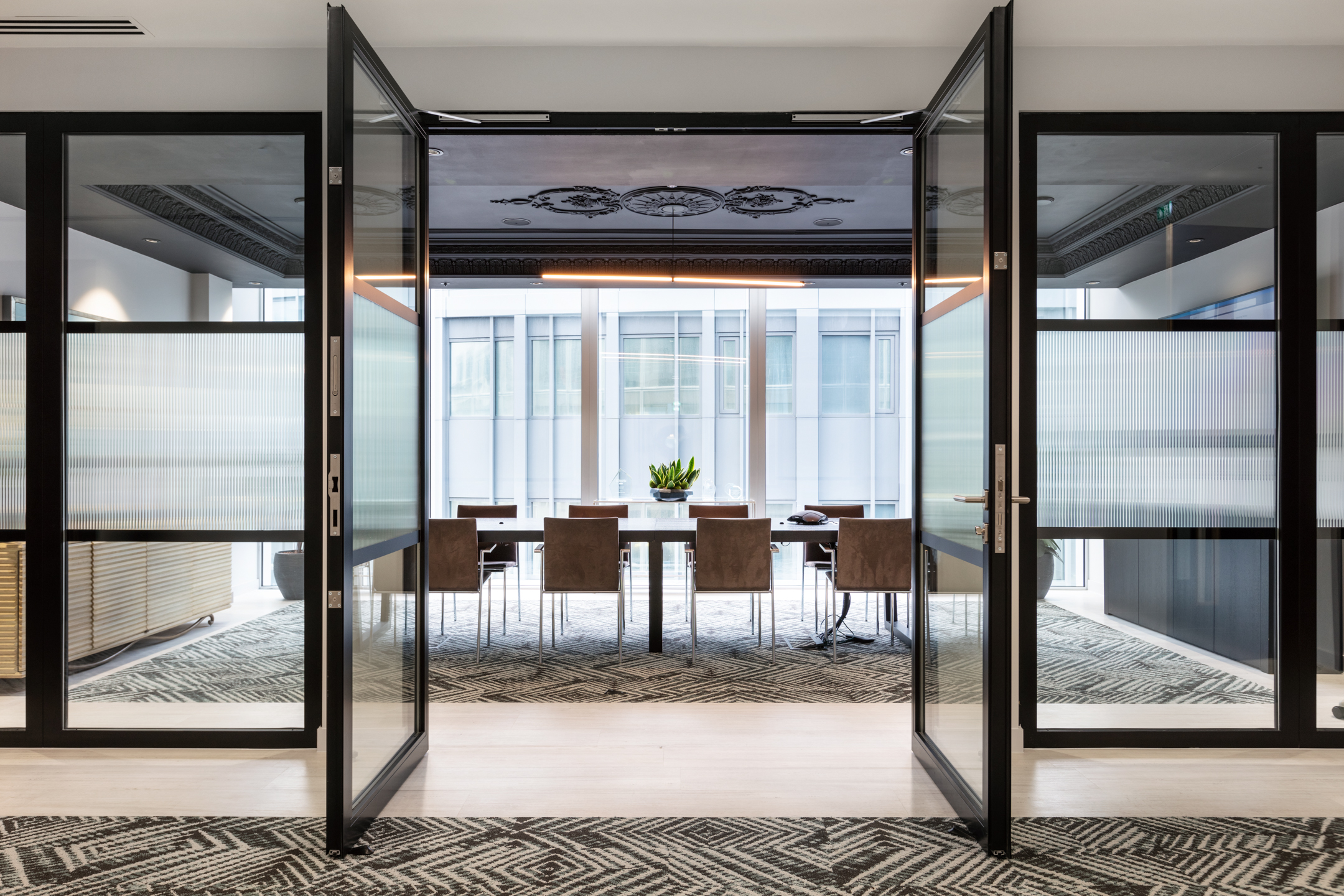 Finncap meeting room with glass double doors leading into a patterned carpeting, modern conference furniture, and a view of surrounding buildings through large windows.