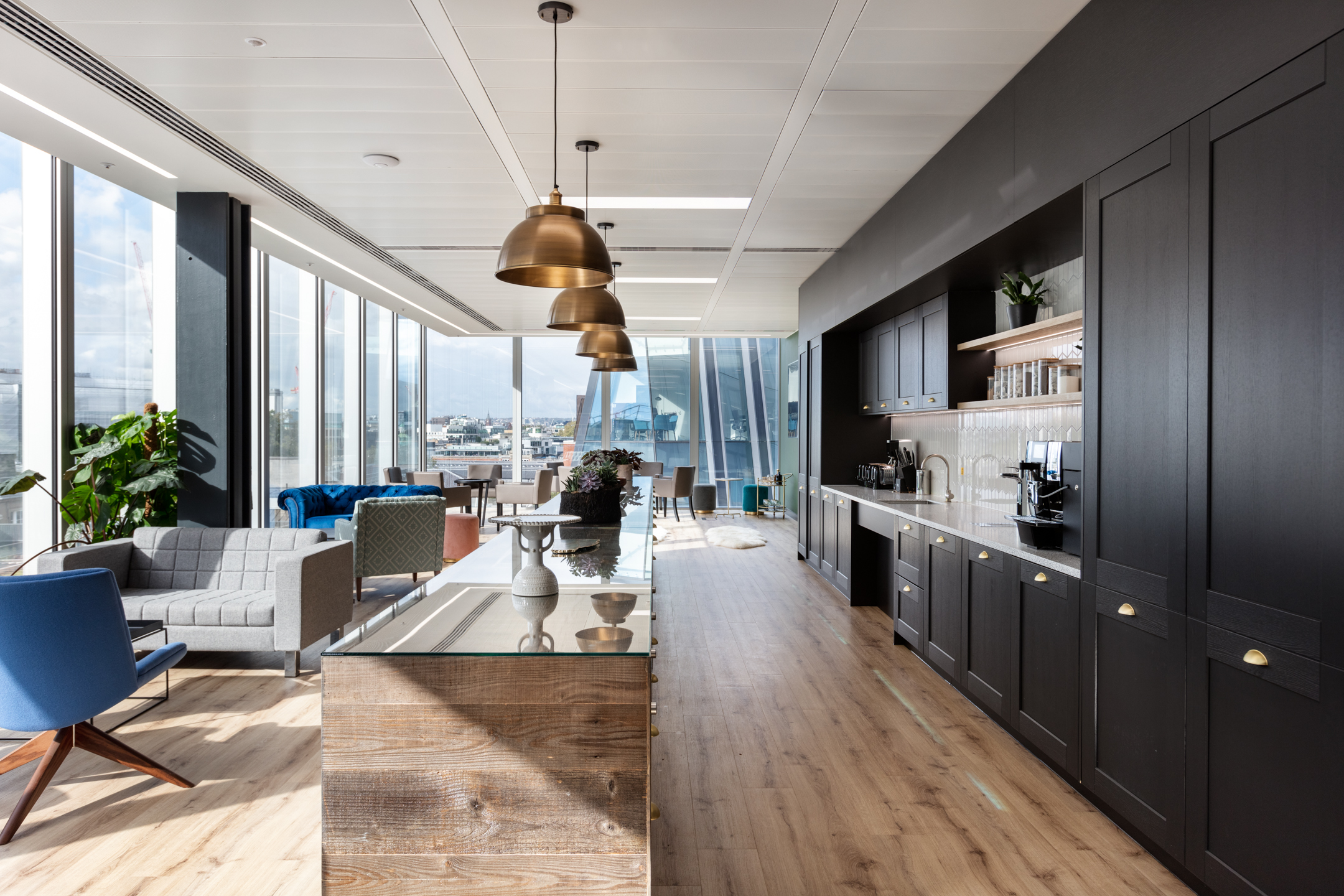 Finncap open-plan teapoint area with a wooden island, dark cabinetry, and comfortable seating near large windows that offer city views.