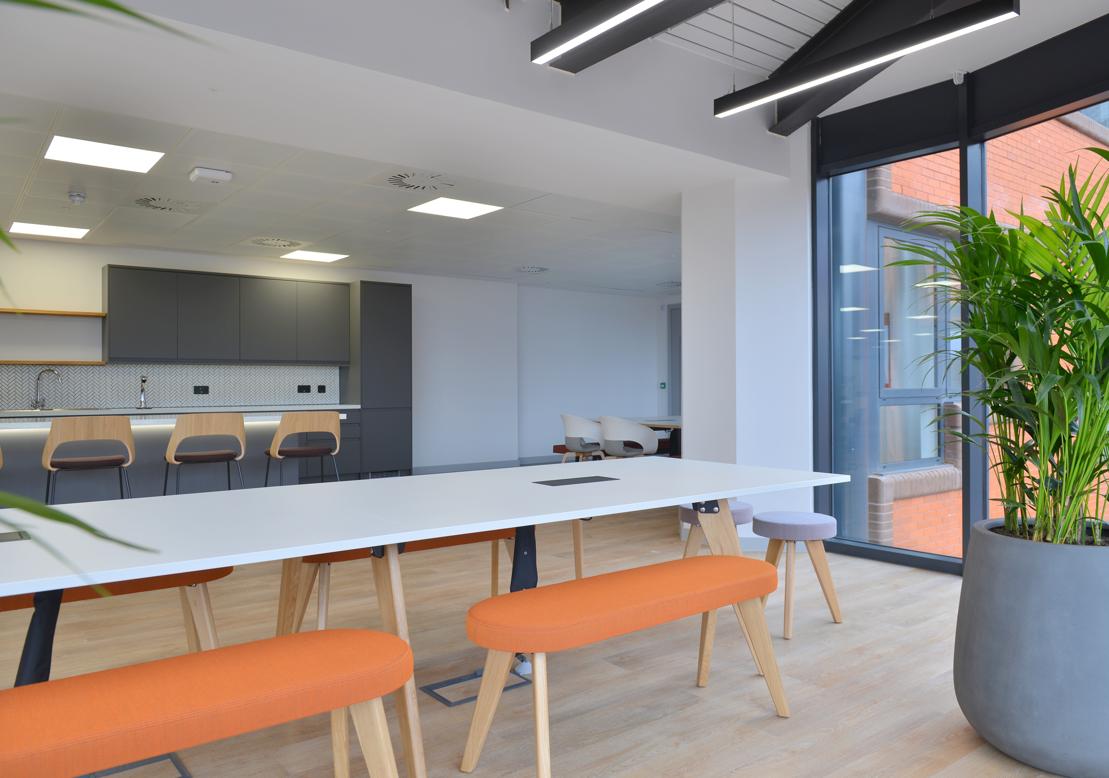 Flexible meeting space with long tables and greenery at Fujitsu Services Edinburgh. Designed by Modus Workspace to create a versatile environment for meetings and informal gatherings.