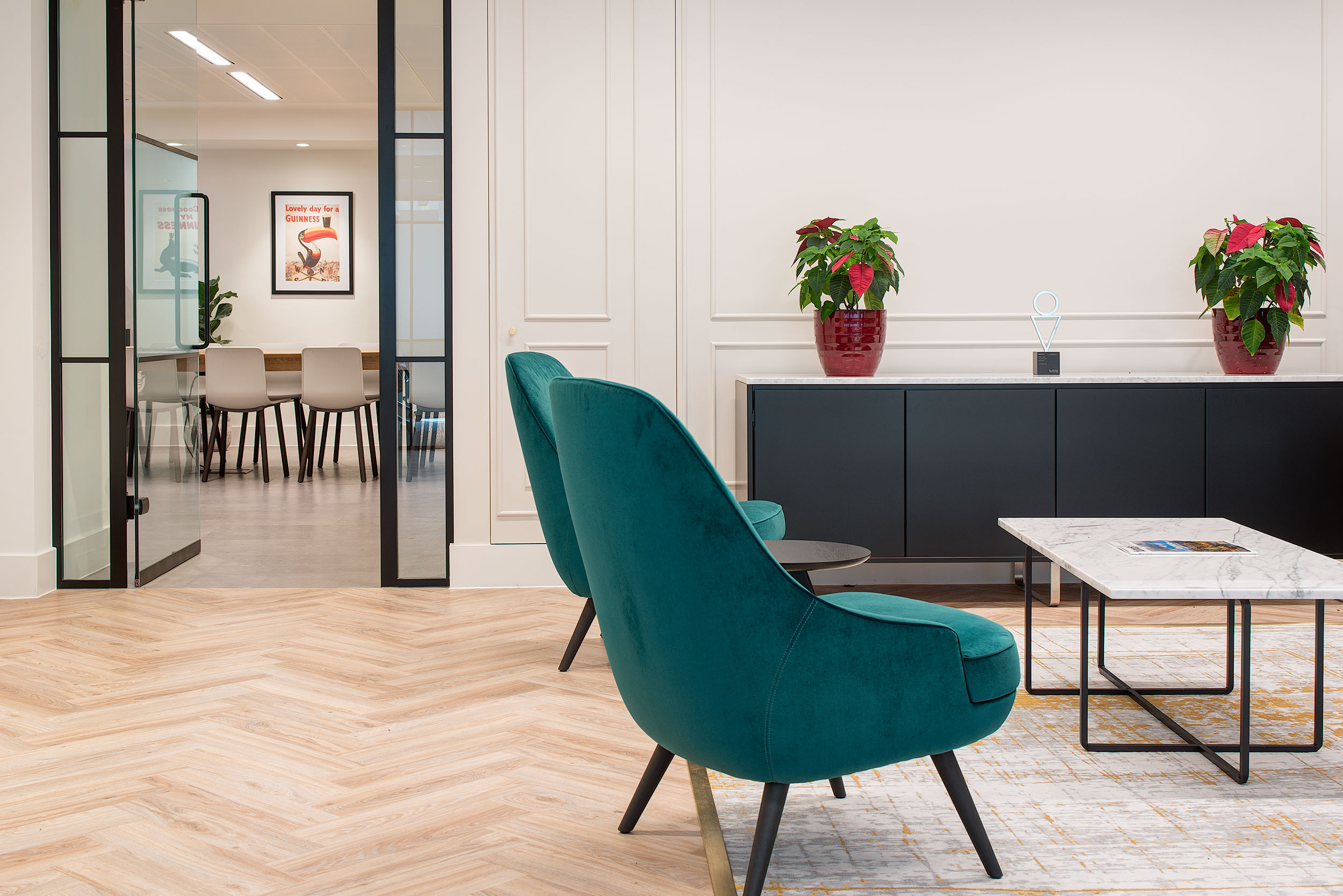 A stylish seating area in Guinness Asset Management's office, designed by Modus Workspace, featuring teal armchairs and a modern coffee table set against a bright, minimalist background.
