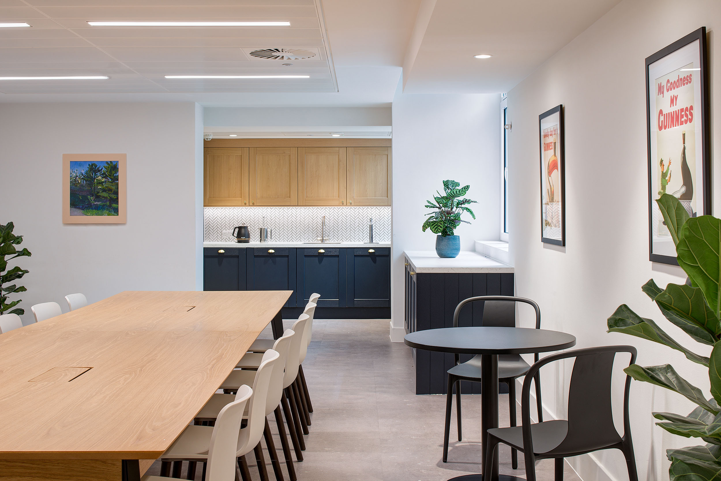 Kitchen and teapoint area in Guinness Asset Management's office designed by Modus Workspace, with a modern kitchen setup, wooden dining table, and ample seating for staff.