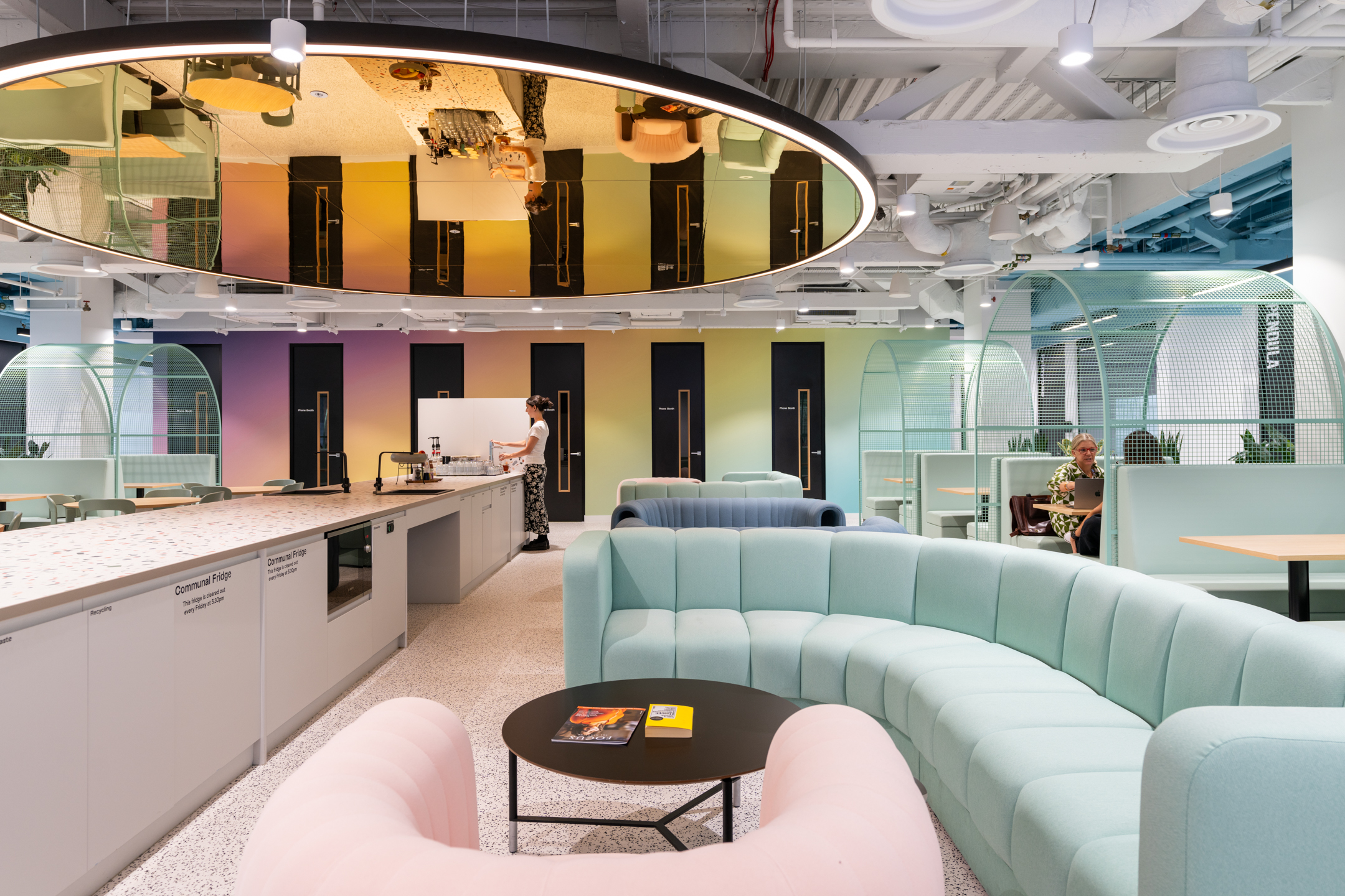 Modus Office Design Guide: A vibrant workspace at Huckletree Bishopsgate featuring pastel-coloured sofas and a modern teapoint area with a mirrored ceiling and communal countertops.