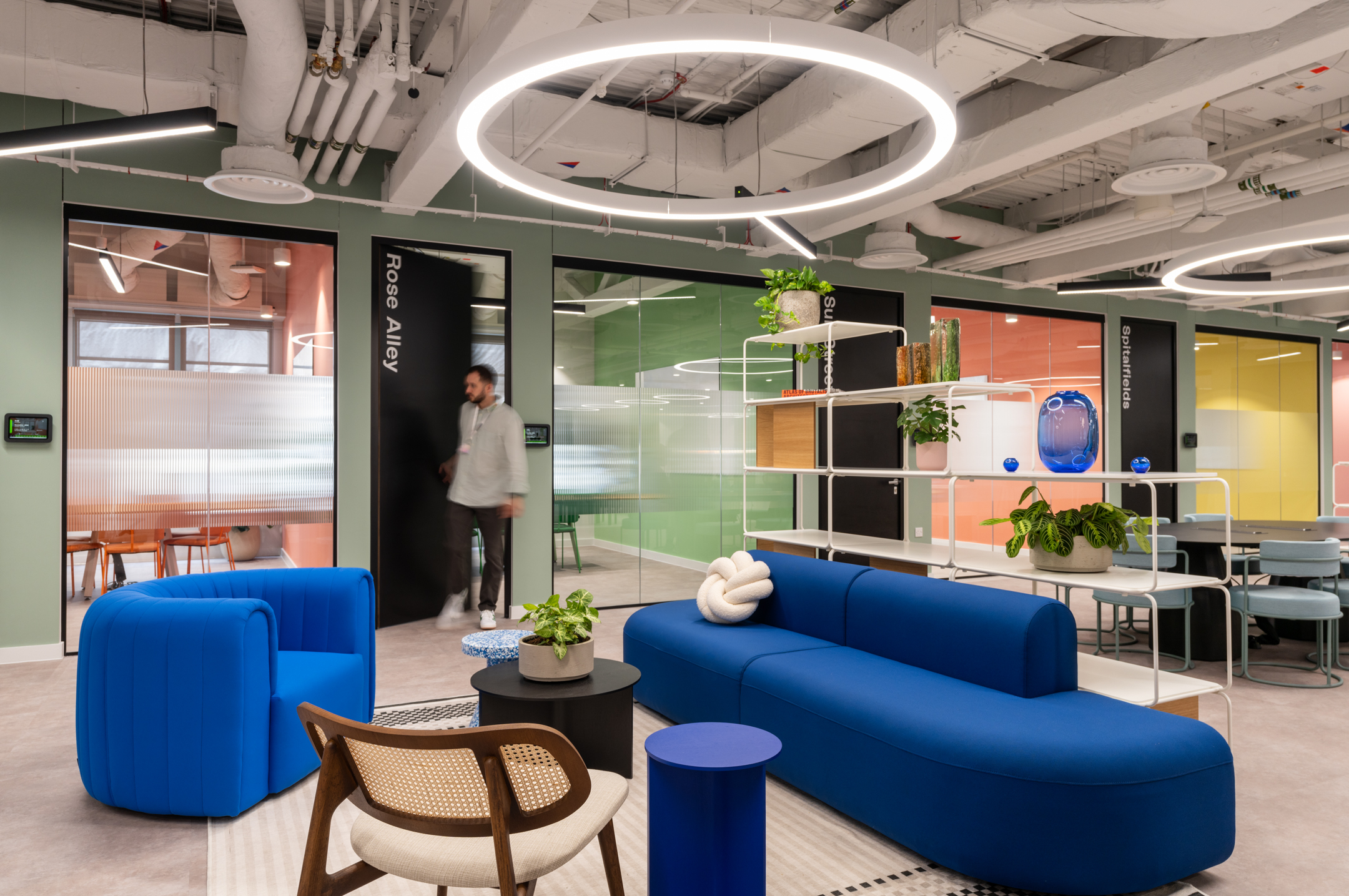Coworking Guide Featured Image: Bold blue seating and soft furniture in a breakout area at Huckletree Bishopsgate, surrounded by glazing partitioned rooms named after London streets.
