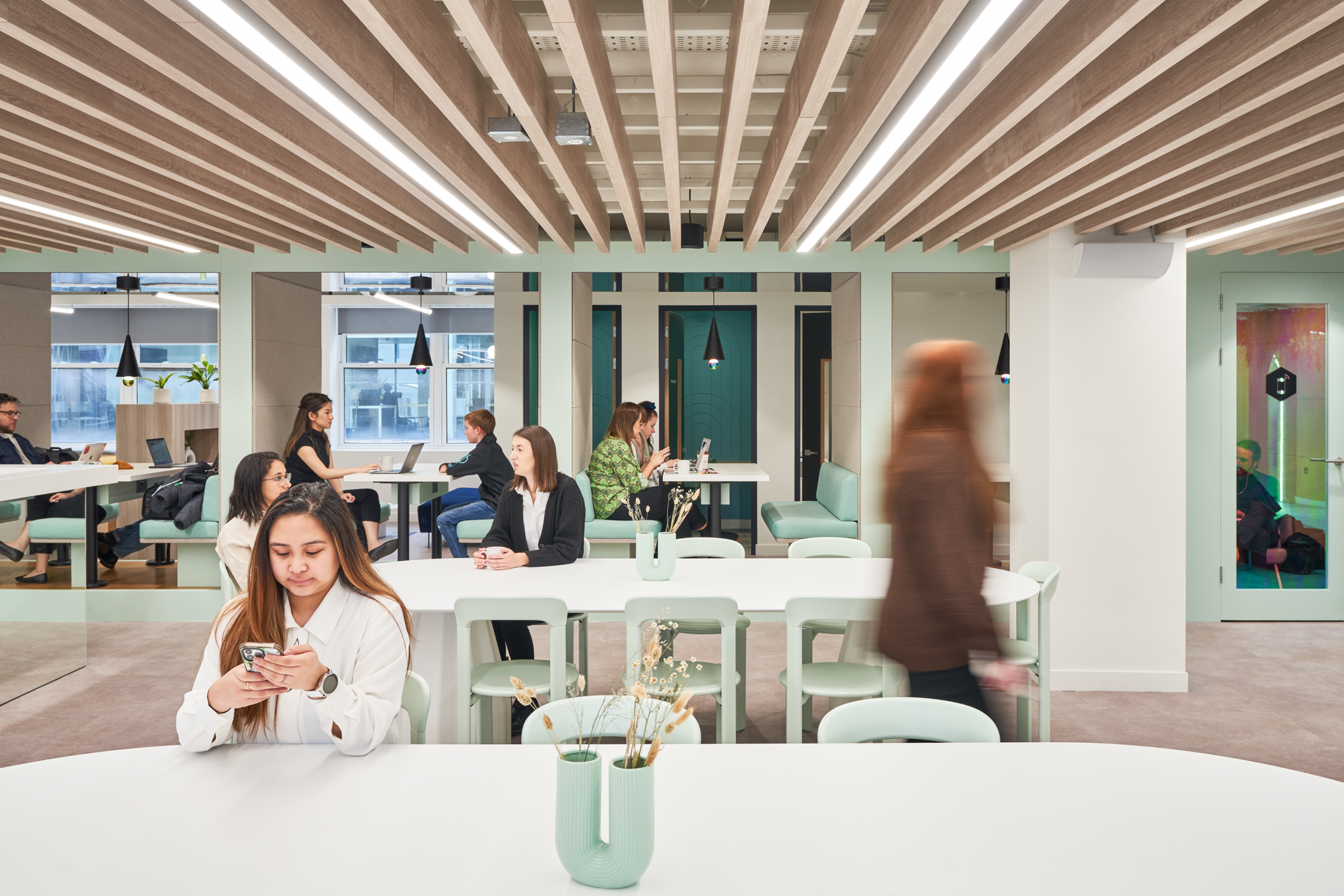 People using various working environments, including booths and communal tables, in Huckletree’s coworking space in Oxford Circus, featuring a light pastel design by Modus.