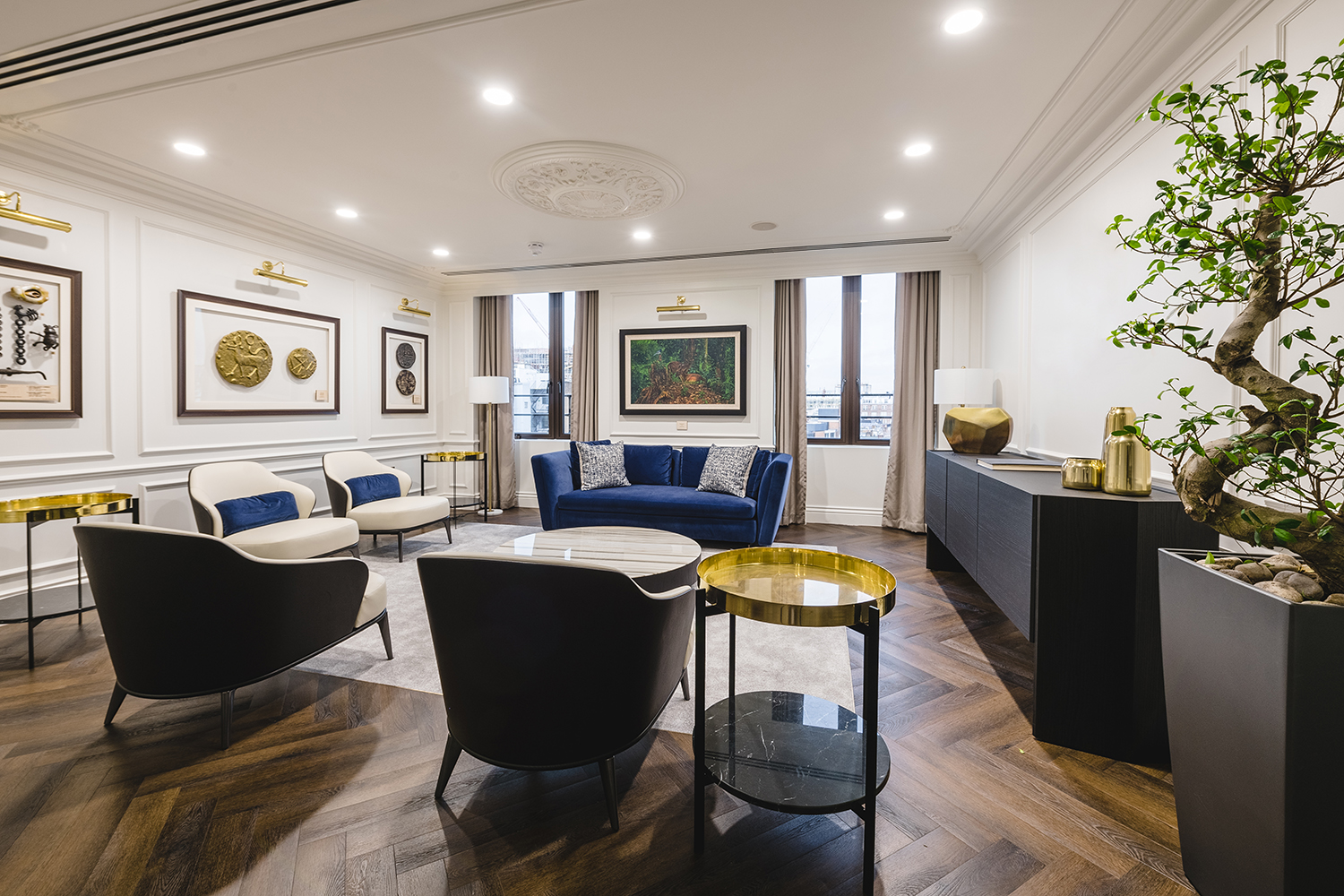 Elegant seating area with armchairs and a blue velvet sofa, framed by gold tables and wall art, in the International Bank's office.