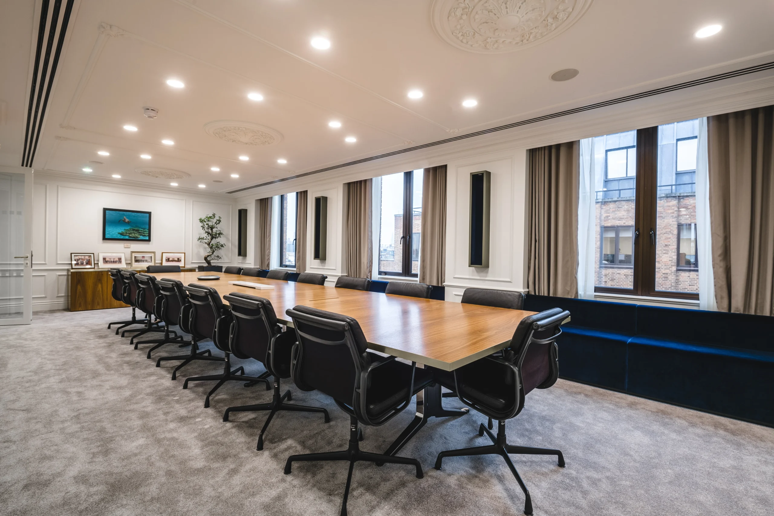 Large boardroom with a long wooden table and black ergonomic chairs, situated under ornate ceiling mouldings.