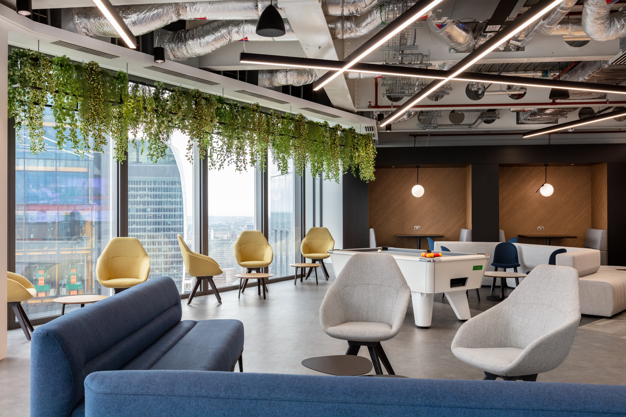 Bright and open breakout space with hanging plants, a pool table, and city views through the floor-to-ceiling windows at the Insurance and Risk Management Firm in Bishopsgate.
