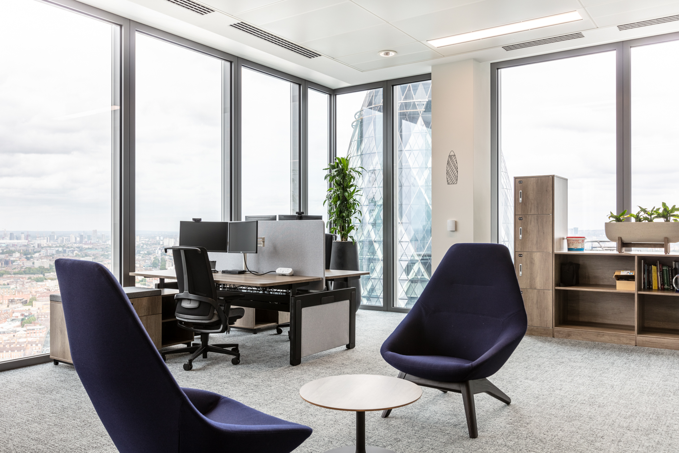 A corner view of the workstations with ergonomic furniture and views of the London skyline, featuring the iconic Gherkin building, at the Insurance and Risk Management Firm in Bishopsgate.