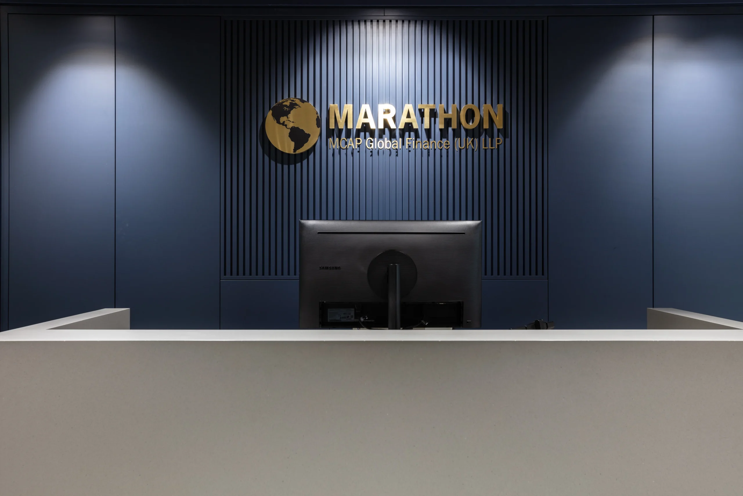MCAP reception area, close view designed by Modus Workspace features a sleek and modern aesthetic with a minimalist reception desk and dark blue accent wall displaying the company logo.
