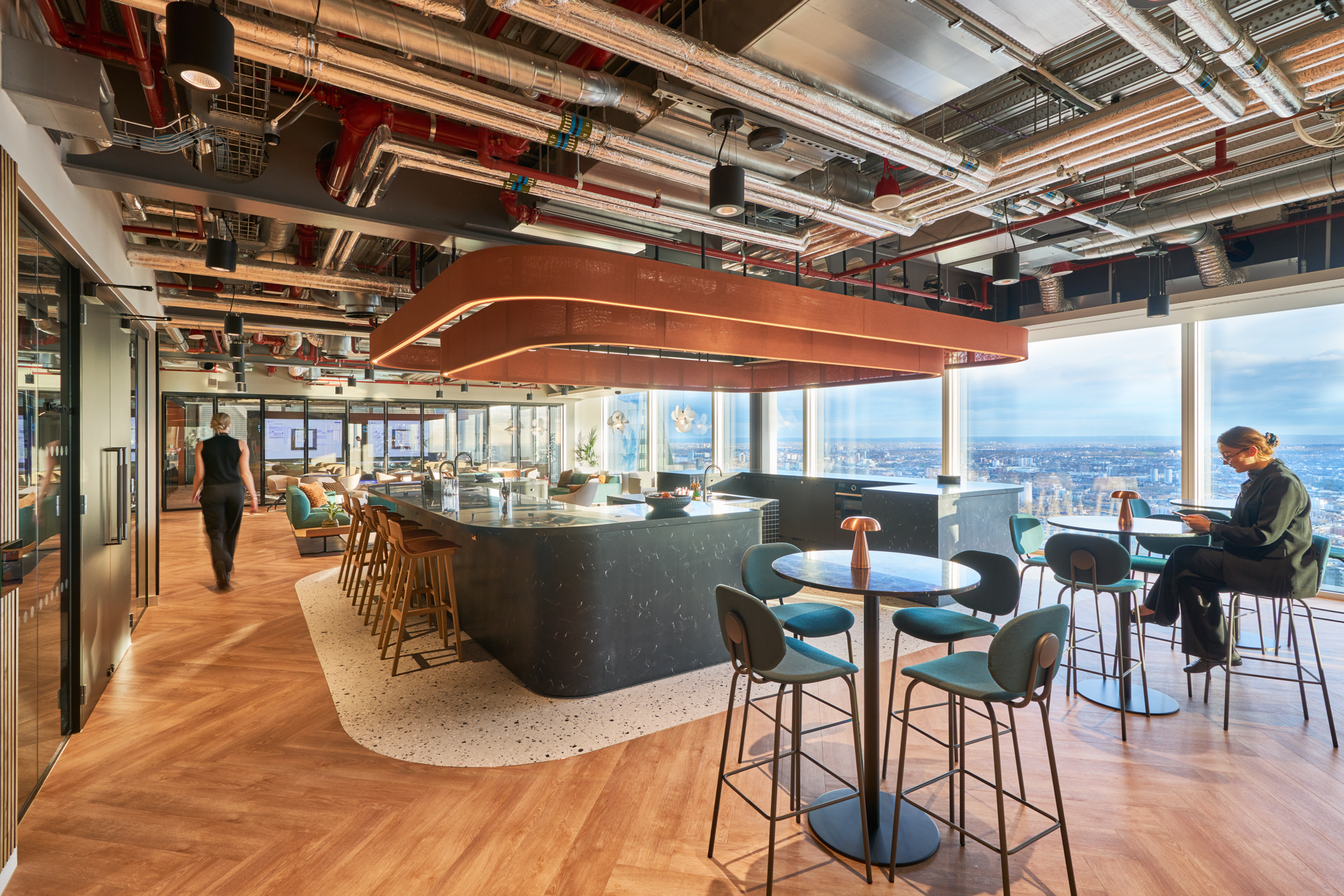 Bentley Systems large and open-plan teapoint with soft seating, overhead hanging halo lights and a glass wall overlooking the rest of the city.