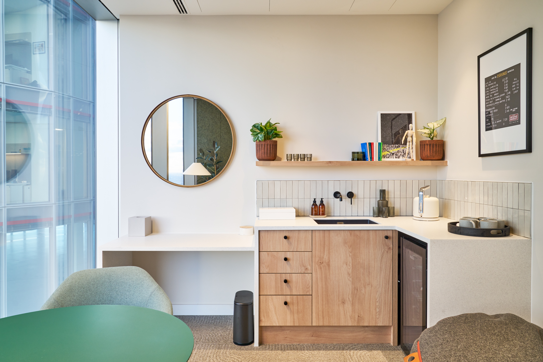 Bentley Systems small meeting room with a small teapoint fitted out with a mini fridge, glasses and mugs and drawers. There is a large mirror and seating area.