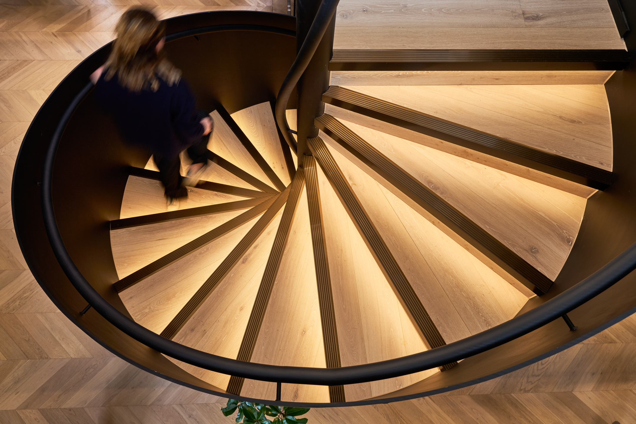 A striking spiral staircase leading from the lower level, part of Lotus's headquarters designed by Modus, showcasing the blend of modern design and historic features from the Ragged School.