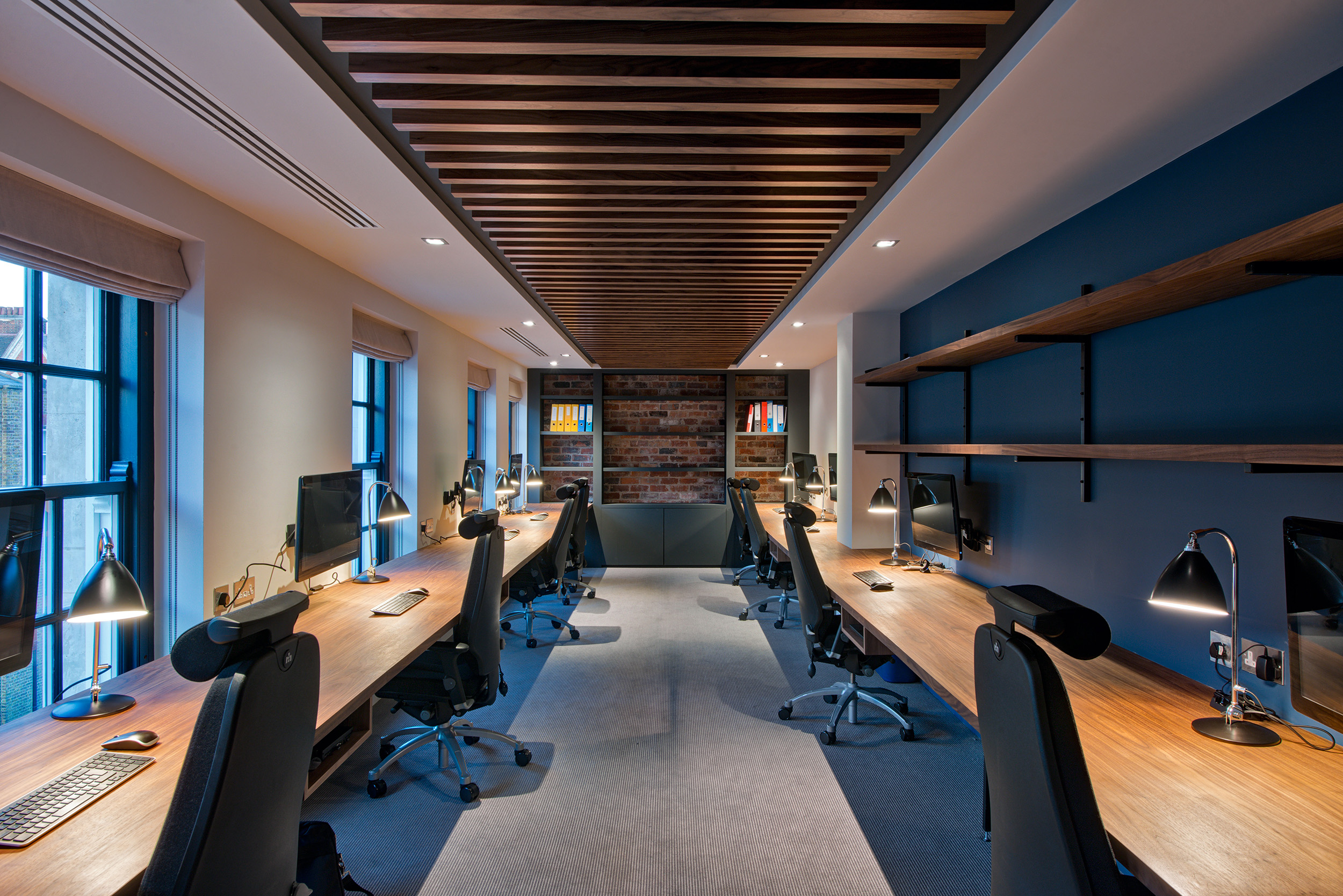 Quiet workspace with individual desks, dark wood accents, and modern lighting design at the private equity firm’s office.