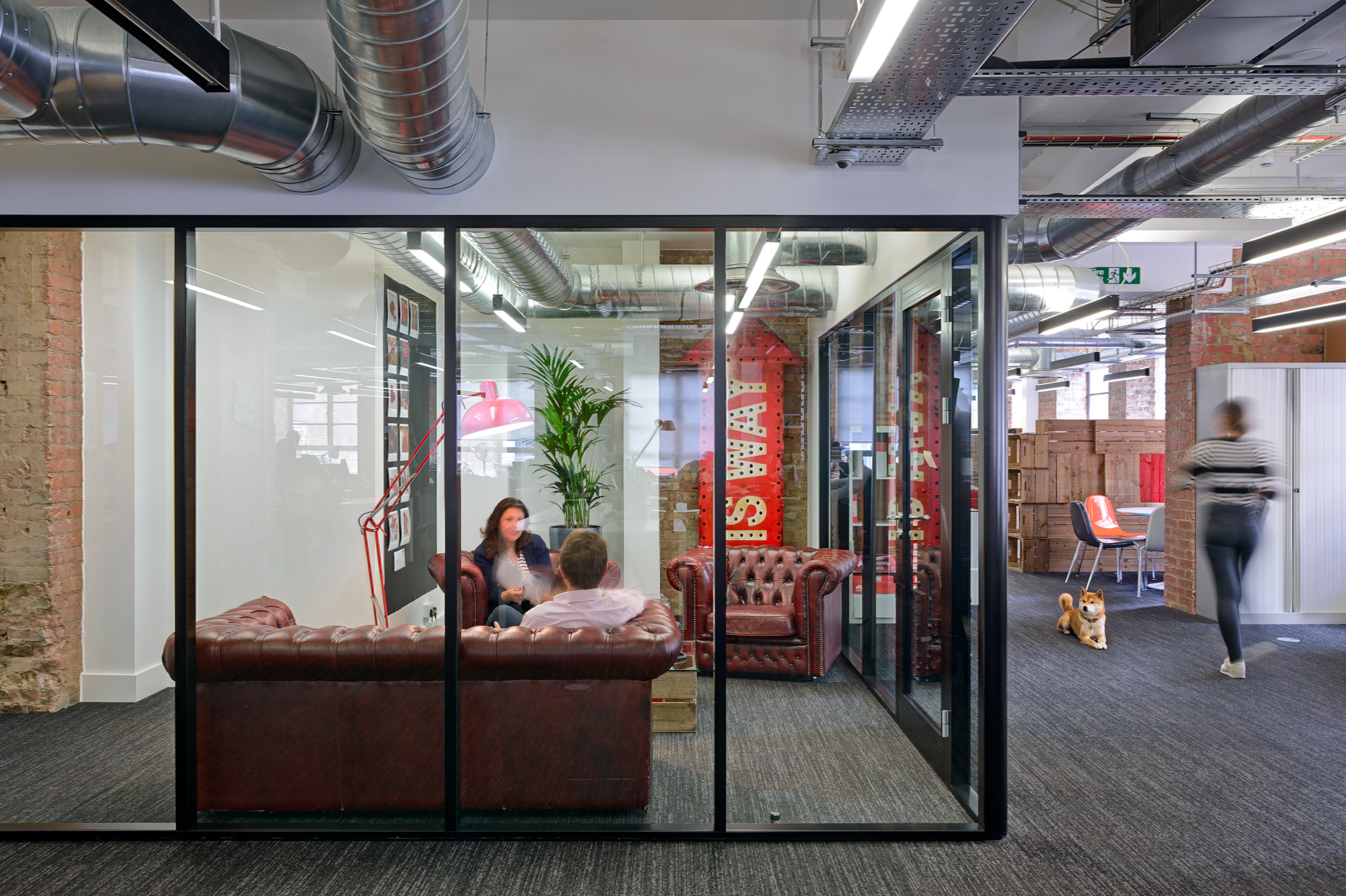 The Red Brick Road office meeting room features glazing partition with leather sofas, industrial decor, and exposed ductwork.