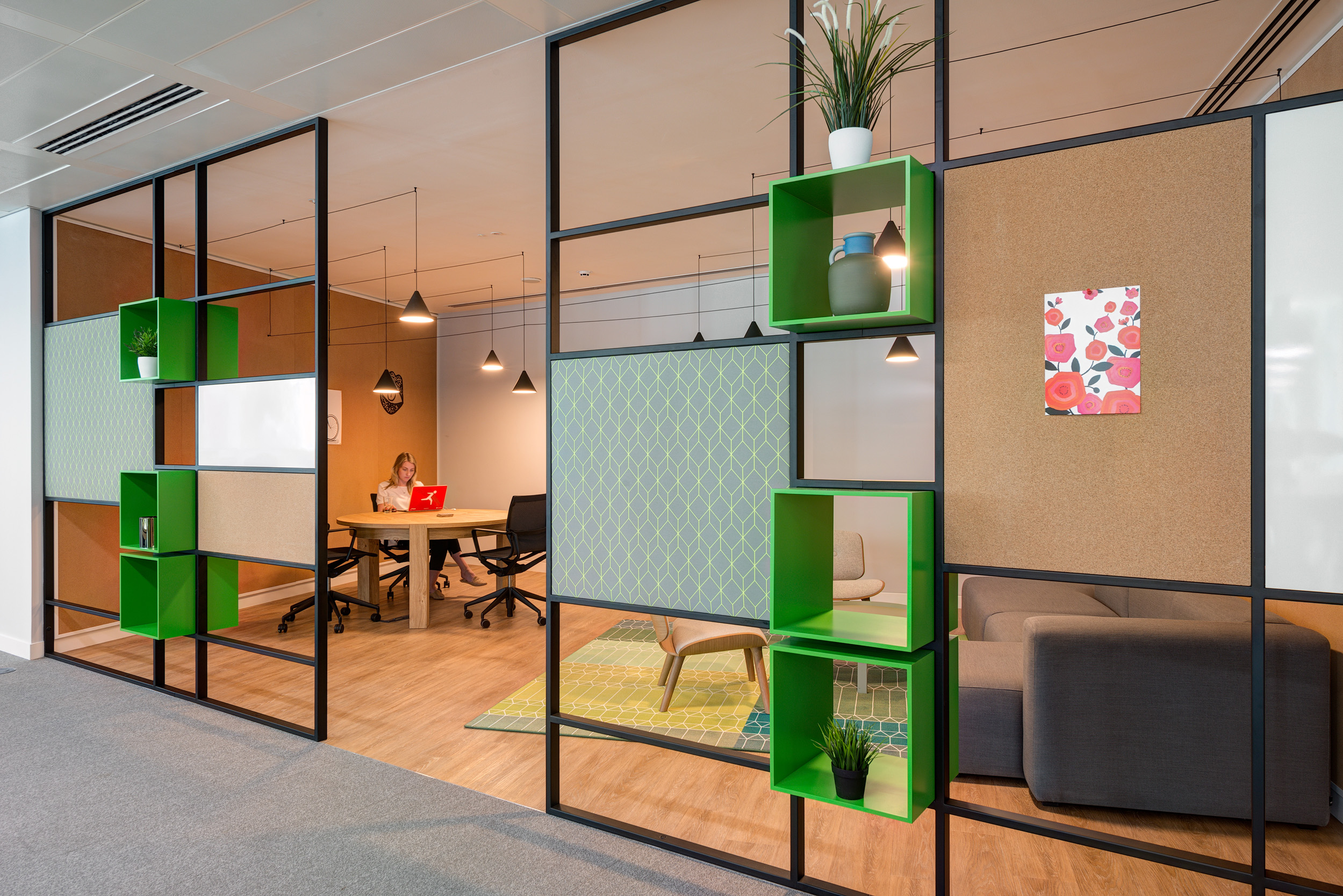 Collaborative workspace at Reply, featuring green shelving, cork panels, and a meeting room designed for flexibility and productivity by Modus Workspace.
