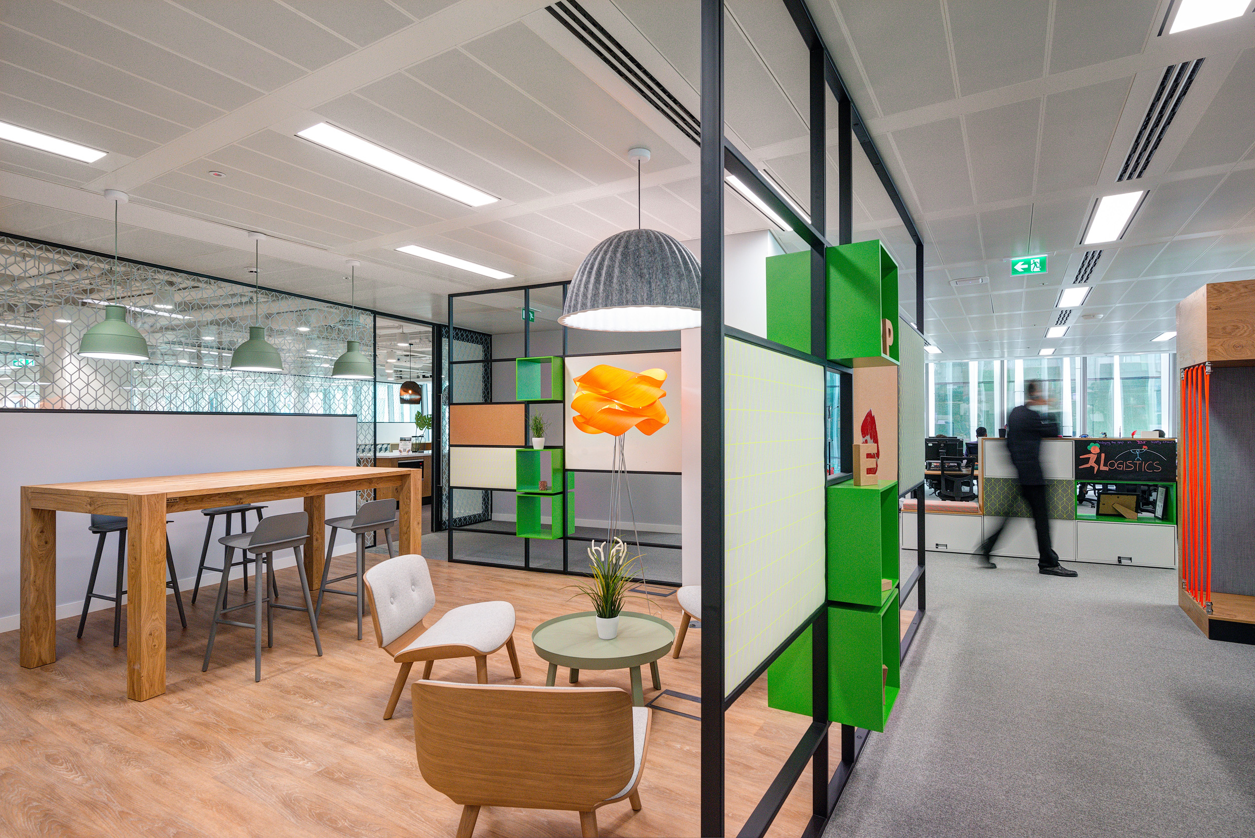 Lounge and breakout area in Reply's office designed by Modus Workspace, with comfortable seating, green shelving, and modern lighting for a relaxing environment.