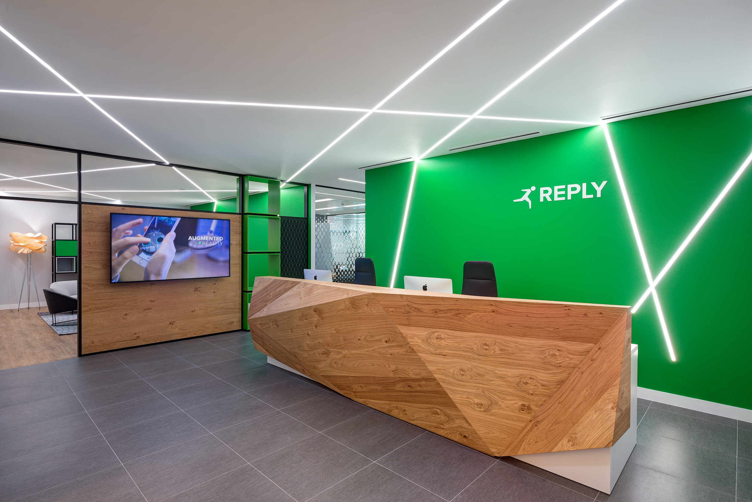 Reception area of Reply's office, designed by Modus Workspace, featuring a striking green wall, geometric wooden desk, and innovative lighting design.