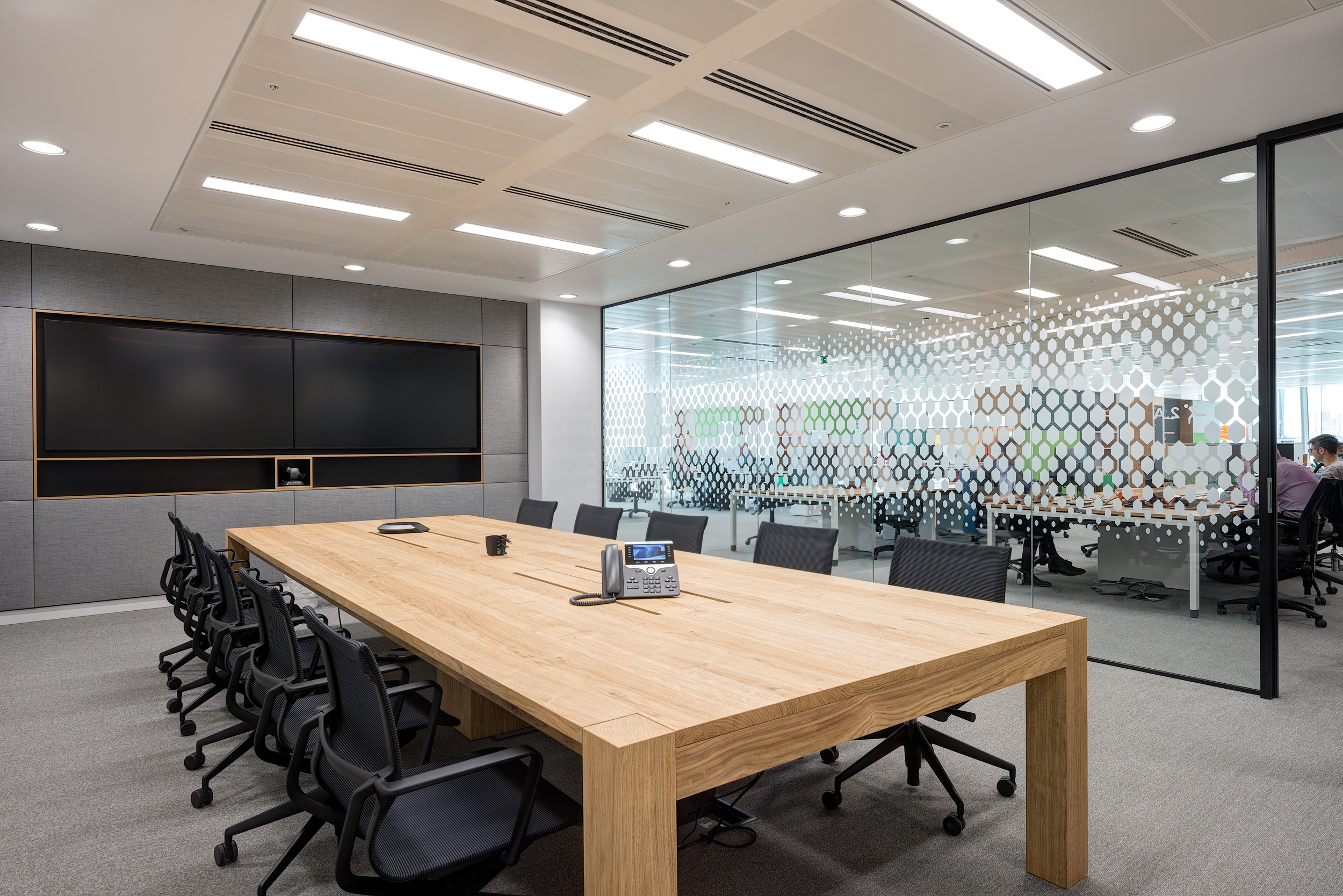 Sleek and modern meeting room in Reply's office designed by Modus Workspace, featuring a large wooden table, black chairs, and glass partitions with geometric patterns.