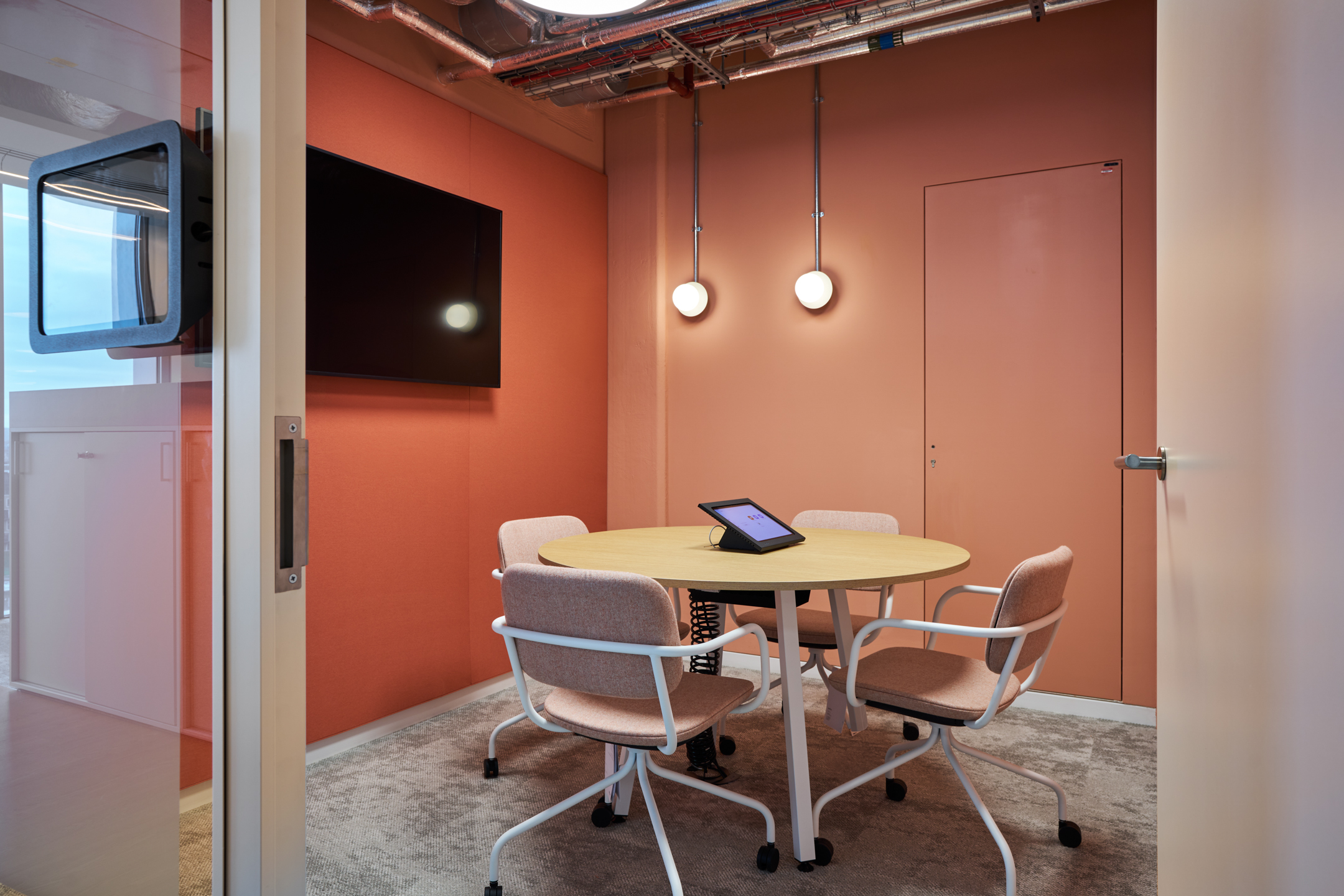 Salesloft small, coral and vibrant meeting room in Salesloft’s London office, designed for focused discussions, with warm colours and modern lighting fixtures.