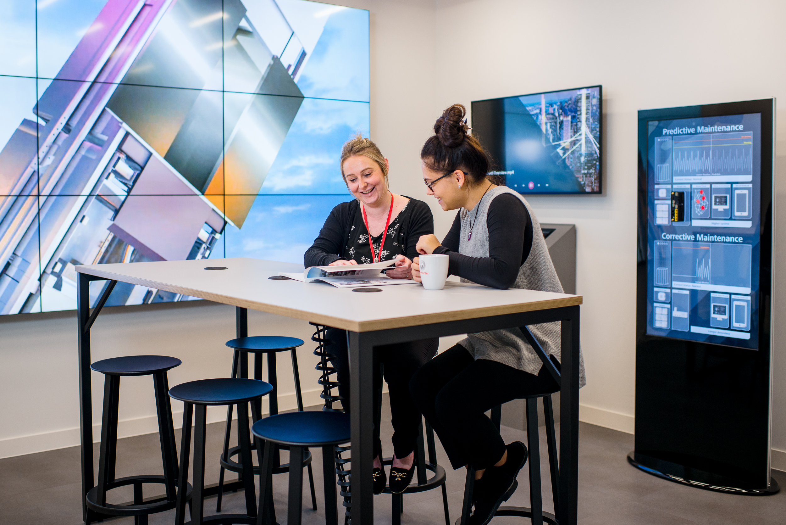 Employees collaborating in Schindler Group's technologically advanced office space, featuring interactive screens and comfortable bar-style seating