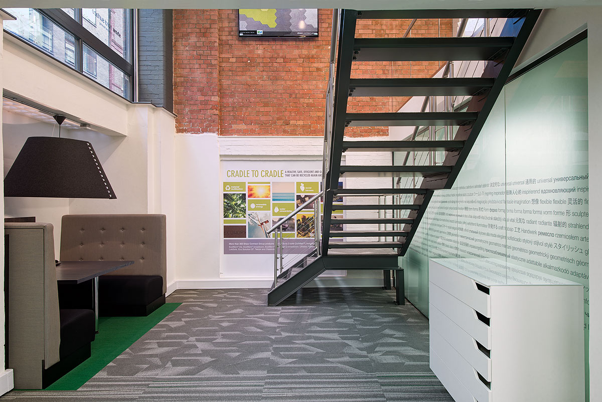 A stairwell leading to private booths in the Shaw Contract Group showroom, with exposed brick and Cradle to Cradle sustainability messaging on the walls.