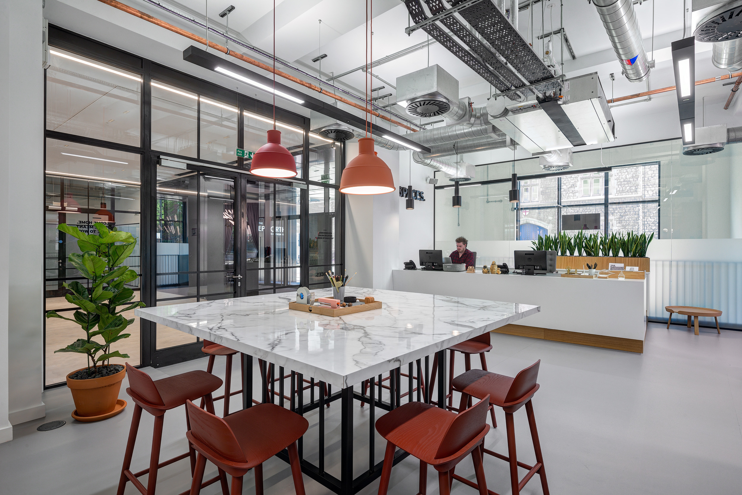 A reception area with a marble-top meeting table, red pendant lights, and orange stools at Spaces Epworth House.
