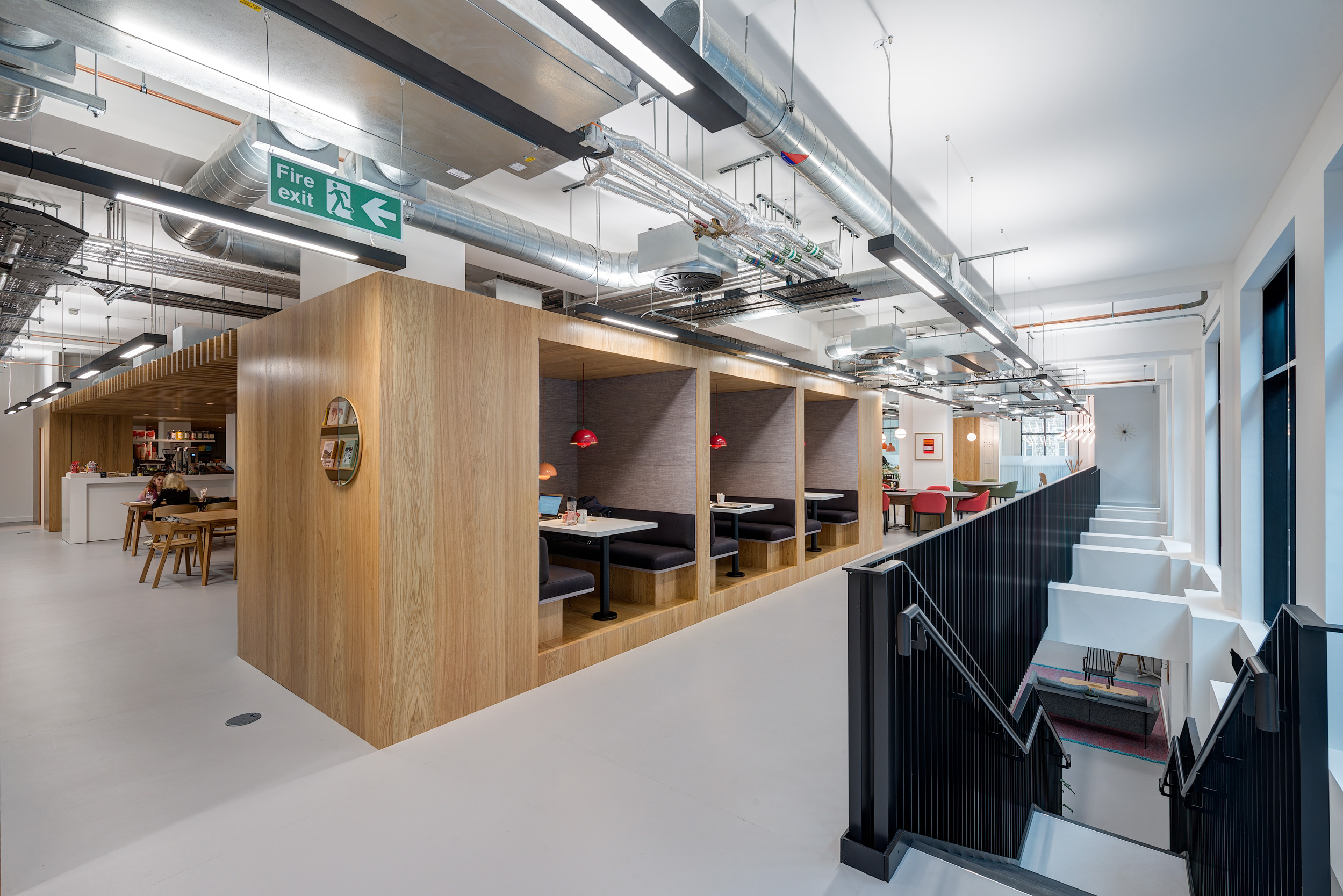 Booth-style seating with wooden dividers and a visible fire exit sign in a contemporary work environment at Spaces Epworth House.