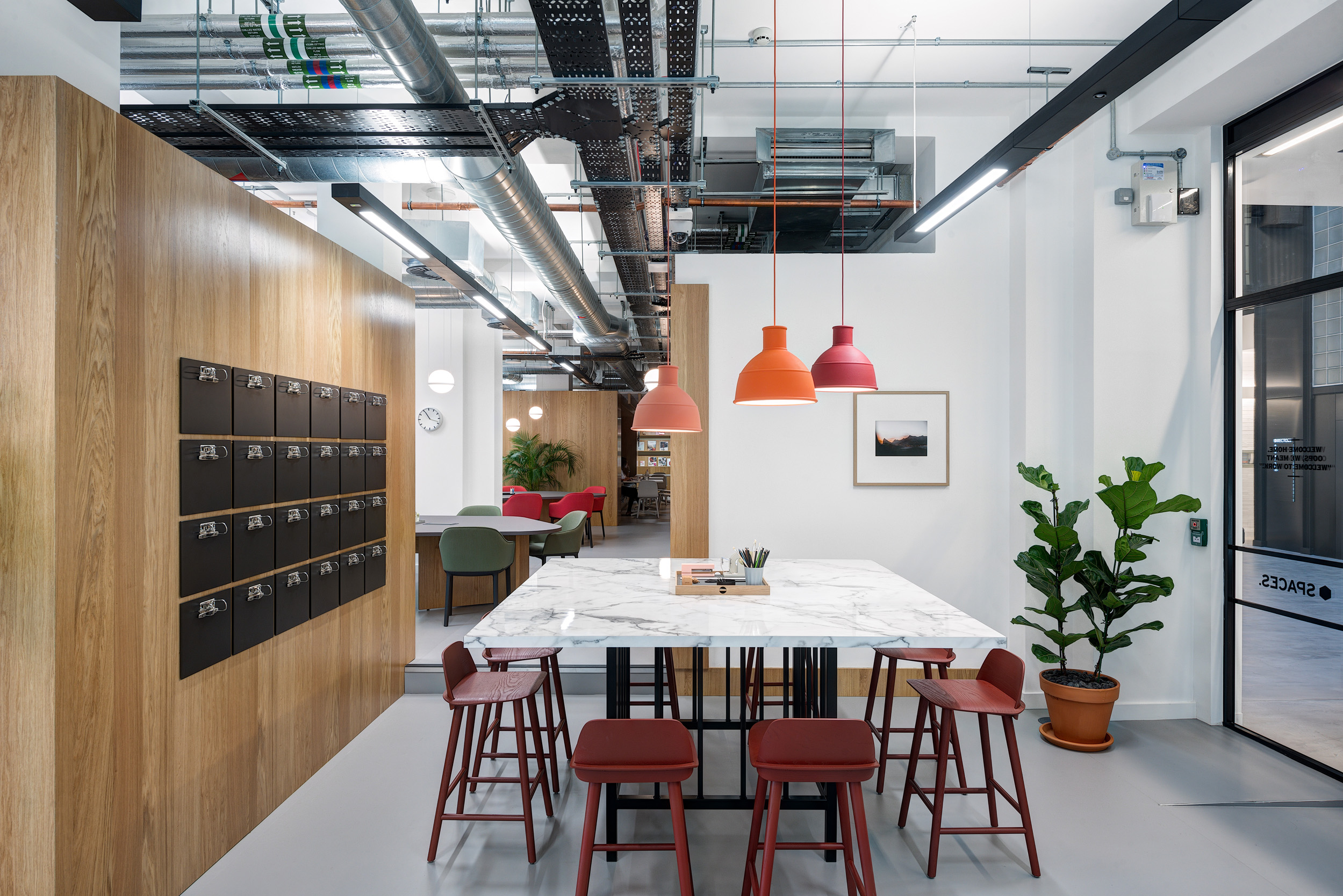 A work area with a marble-top table, red and orange pendant lights, mailboxes on the wall, and green plants at Spaces Epworth House.