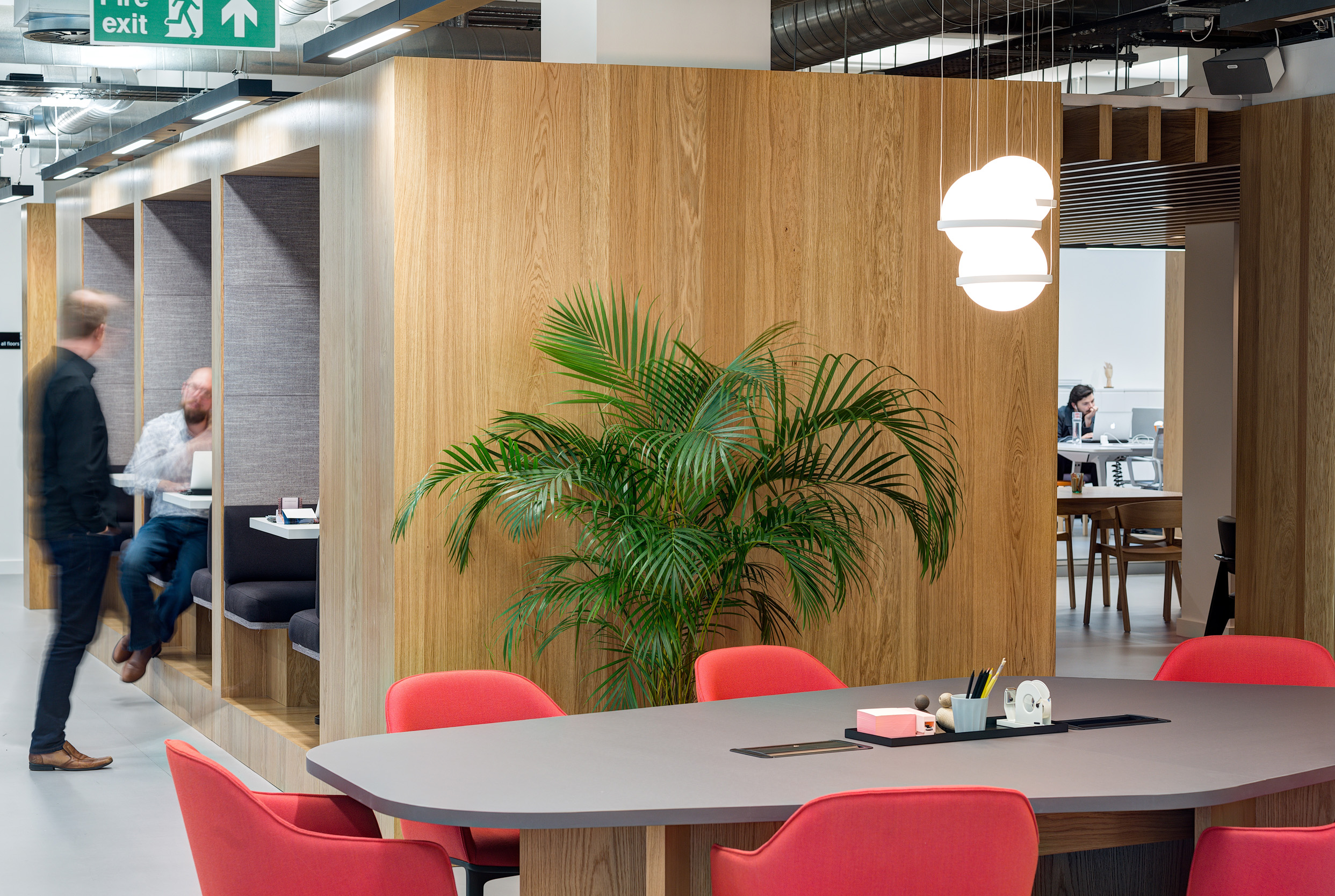 A breakout area with a central table, red chairs, and wooden wall panels, adjacent to booth seating in Spaces Epworth House.