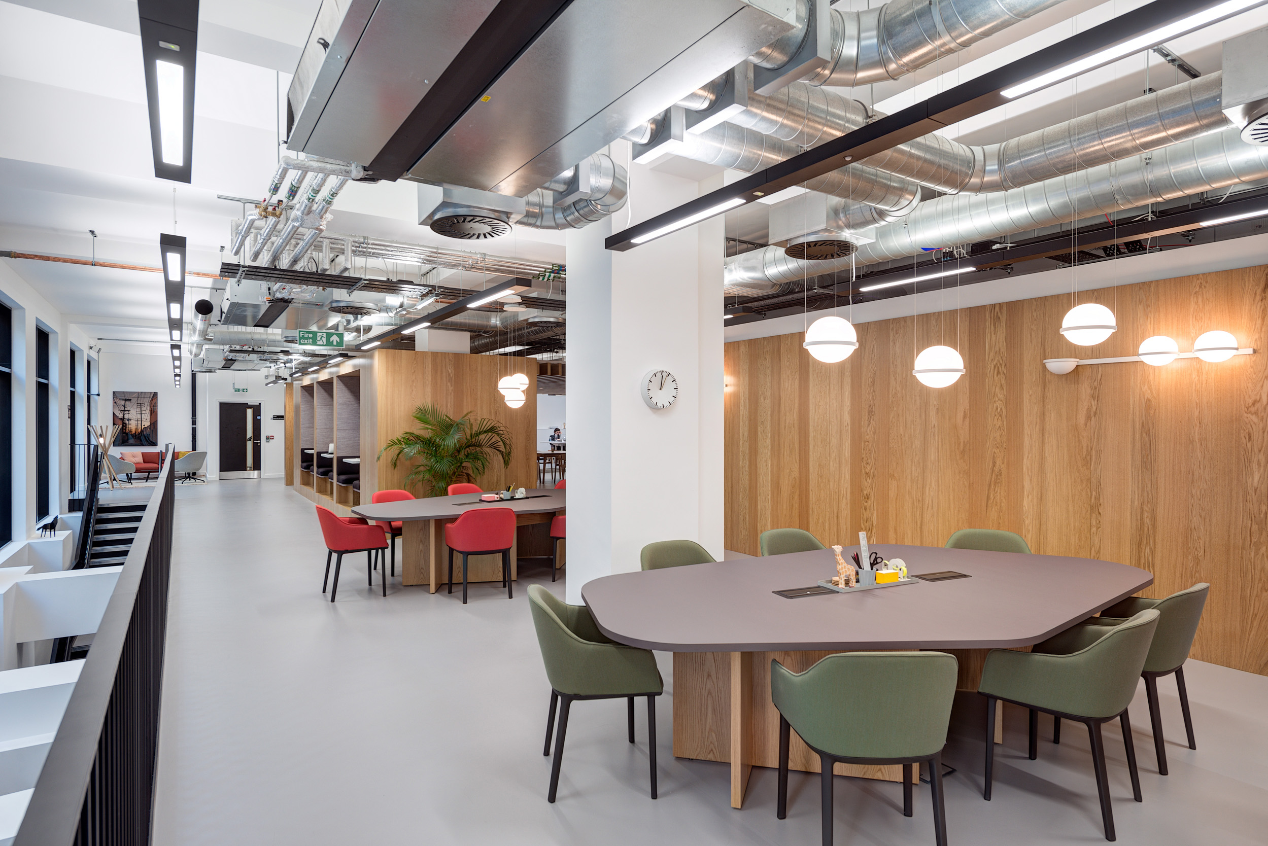 A workspace featuring a large central table with green chairs, pendant lighting, and exposed ceilings in Spaces Epworth House.