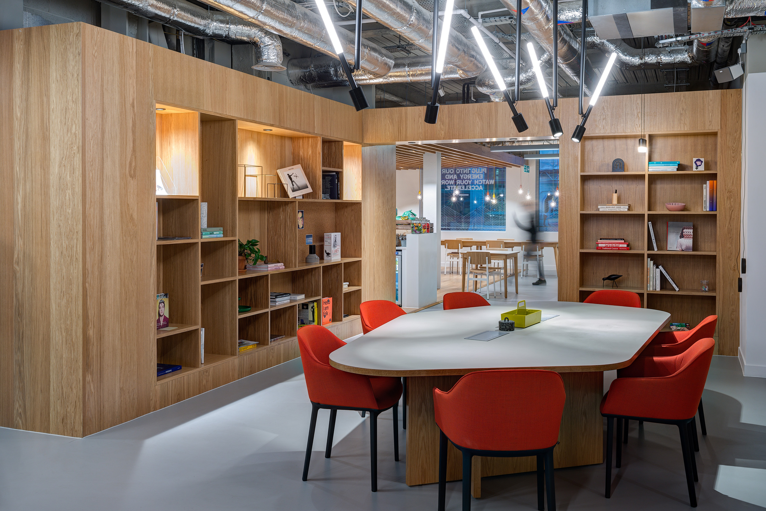 A meeting area with red chairs and a pentagon table, surrounded by shelving and industrial lighting at Spaces, 30 Moorgate.