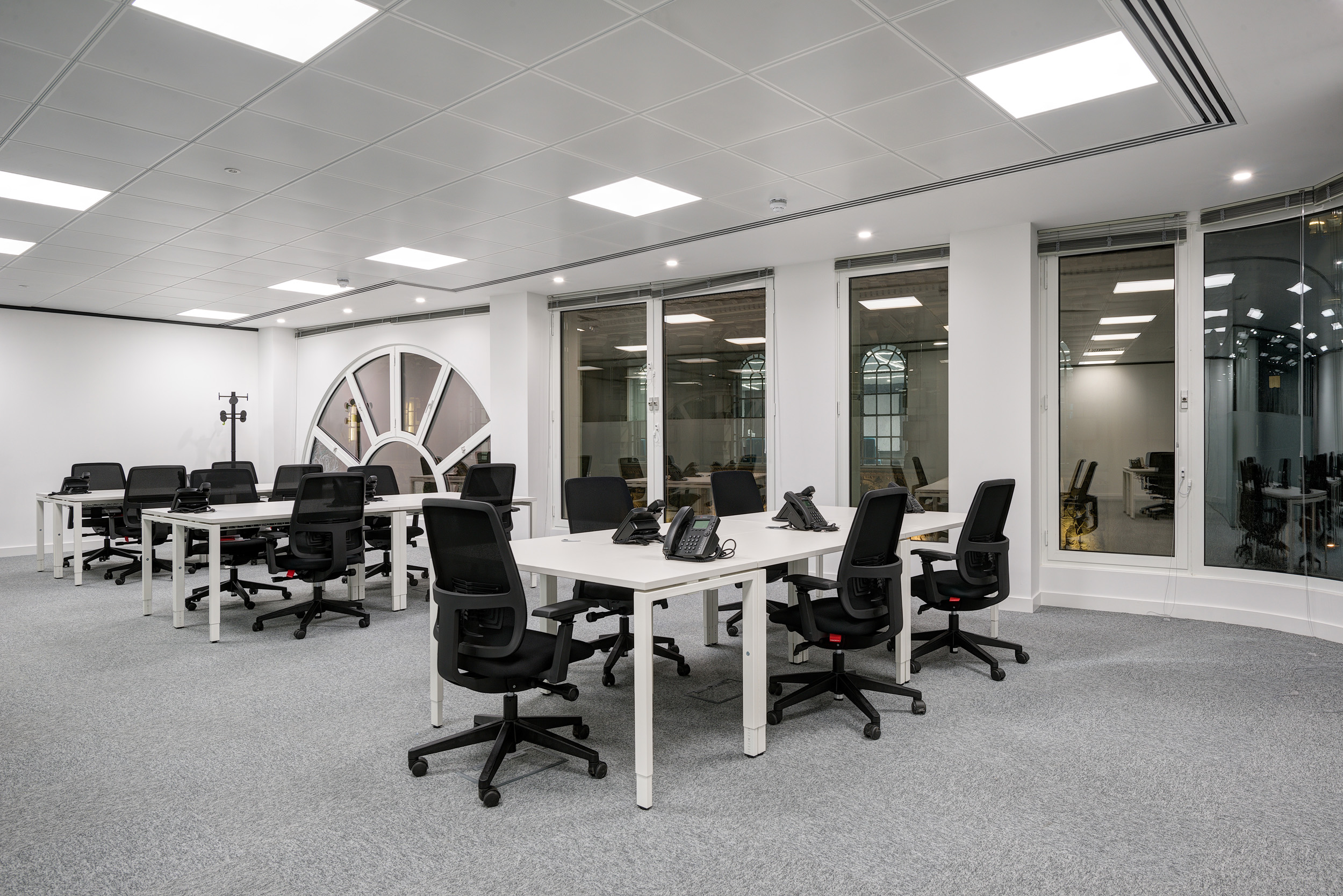 An open-plan office with large arched windows, white desks, and ergonomic black chairs at Spaces, 30 Moorgate.
