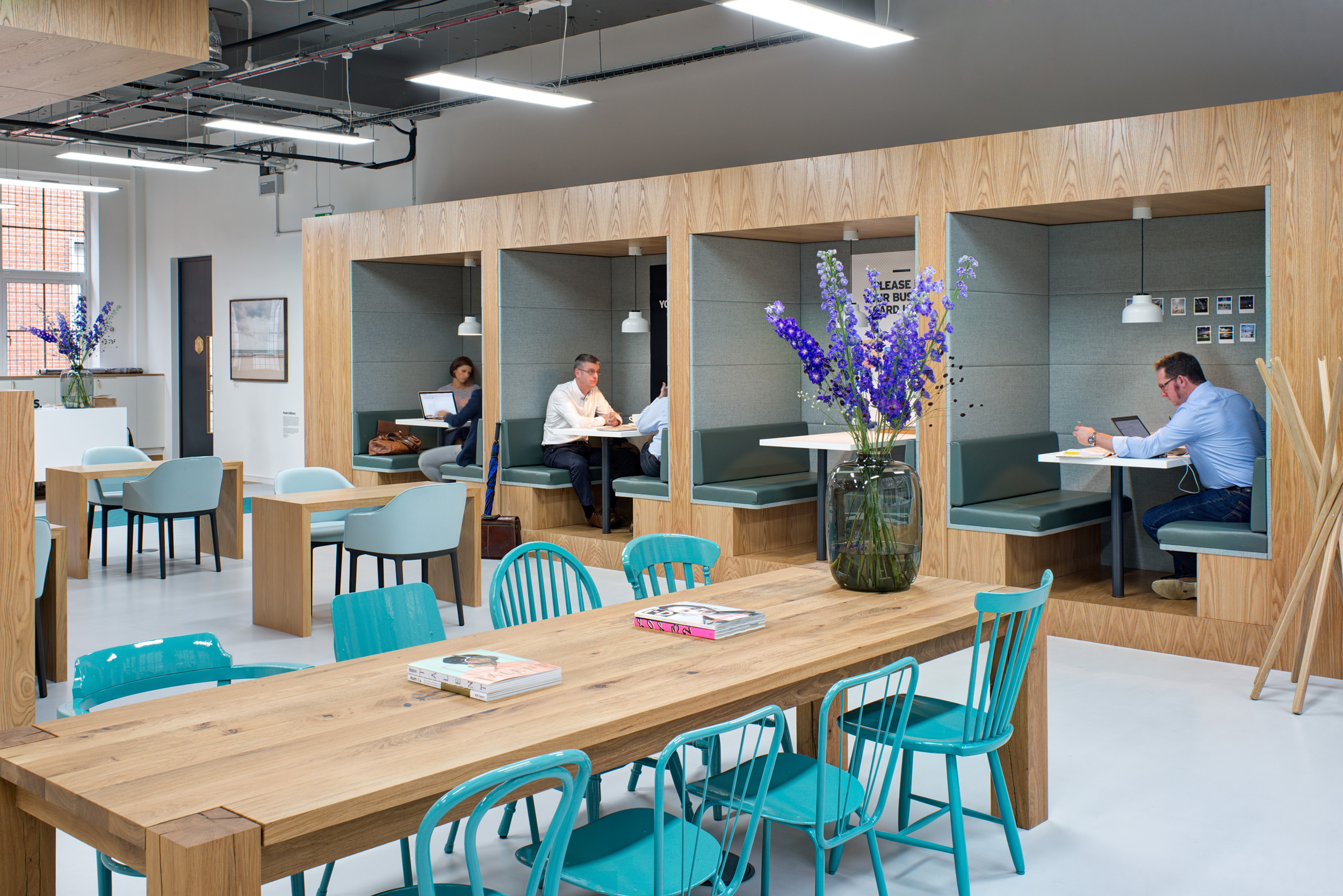 Booth seating and communal wooden tables, with flowers and books, in the collaborative area at Spaces, Oxford Street.