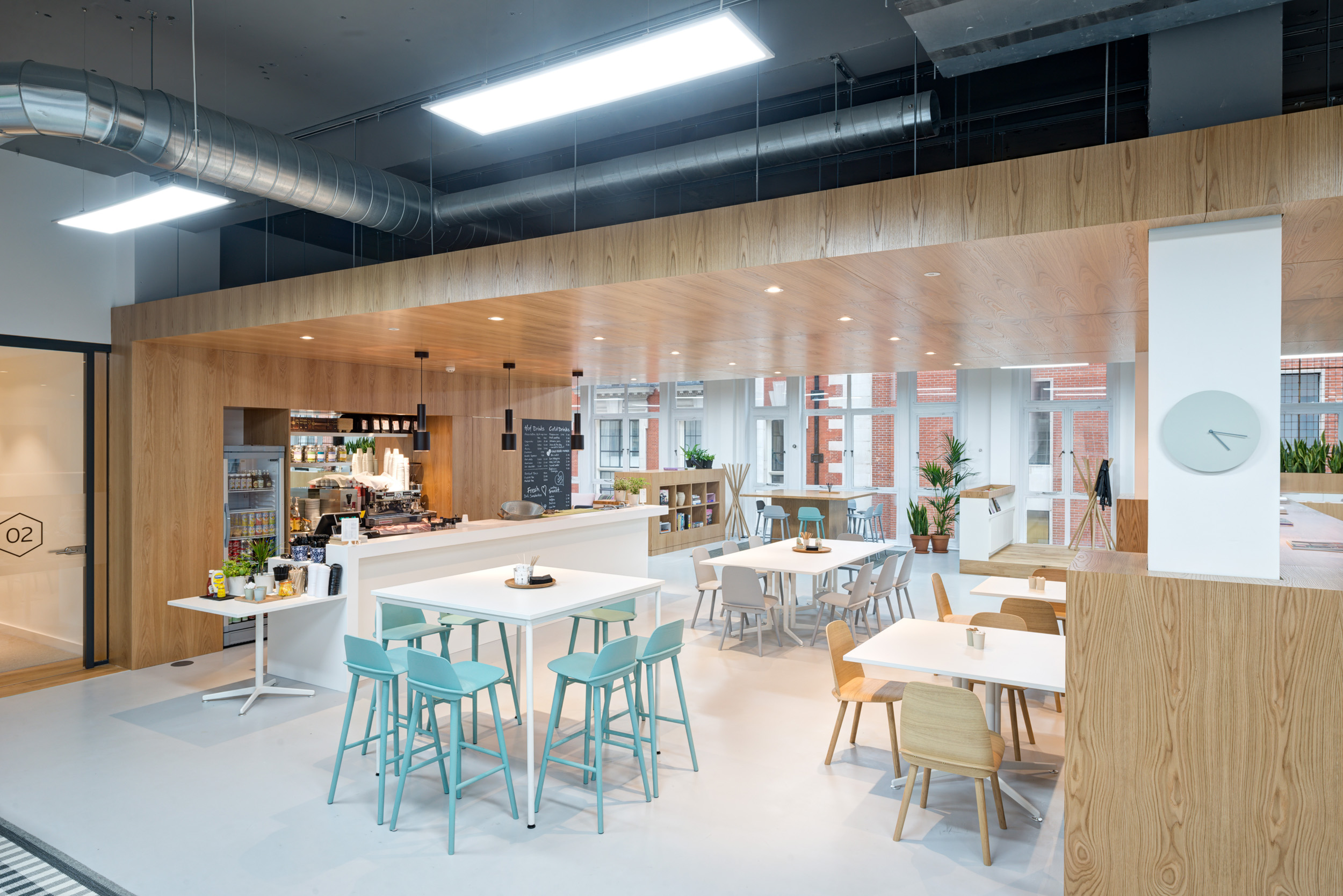 Teapoint and cafe area with wooden tables and highchairs, surrounded by potted plants and bright lighting at Spaces, Oxford Street.