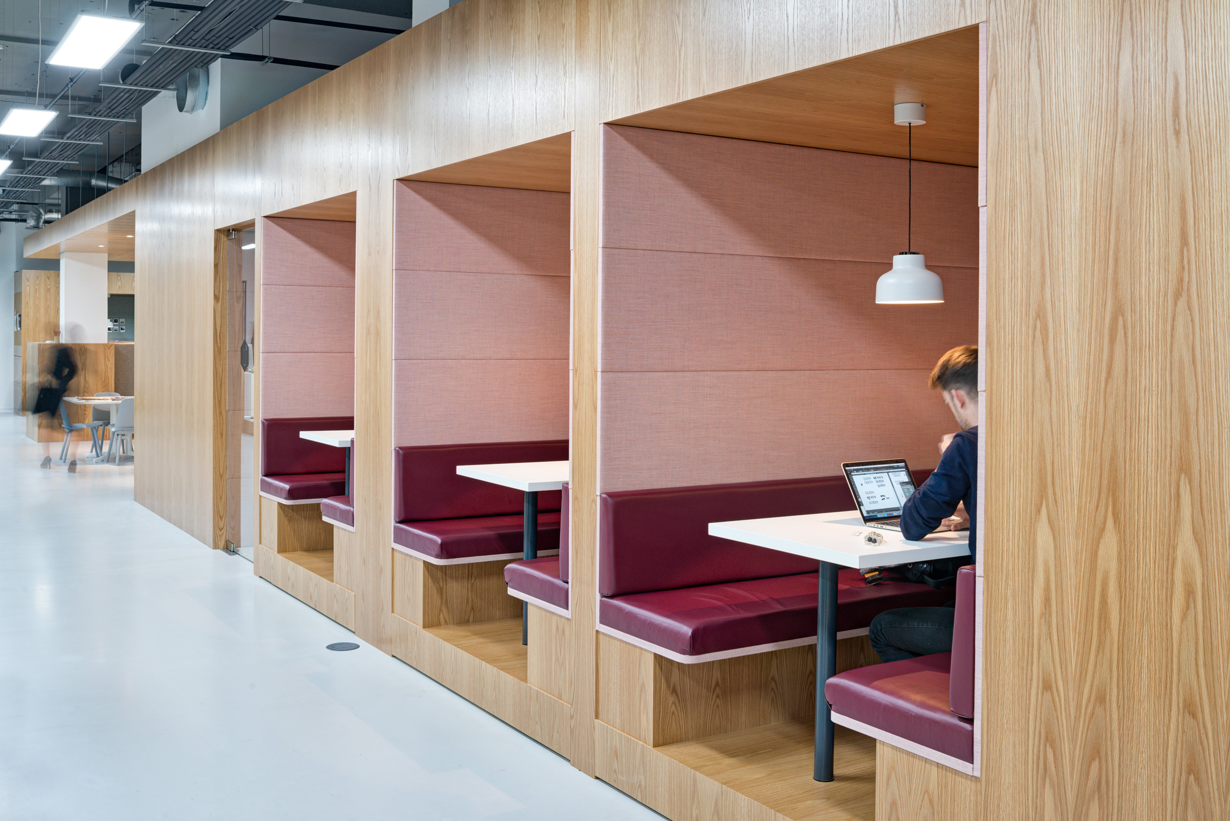 A row of private booths with overhead lighting, surrounded by a minimalist wooden design in the interior of Spaces, Oxford Street