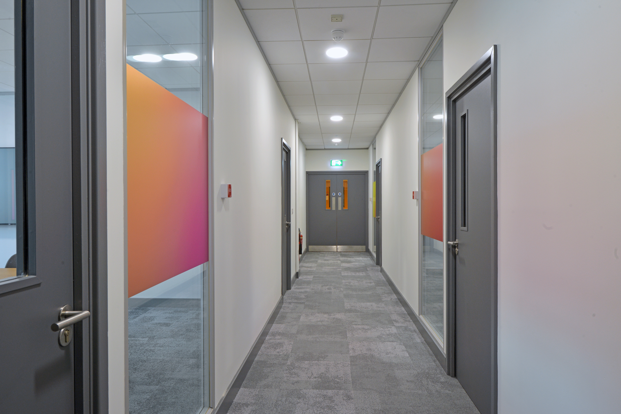 Warrington hallway at Fujitsu Services Warrington with vibrant gradient panels on the windows, enhancing the office’s modern and bright aesthetic. Designed by Modus Workspace to improve the flow and connectivity of the space.
