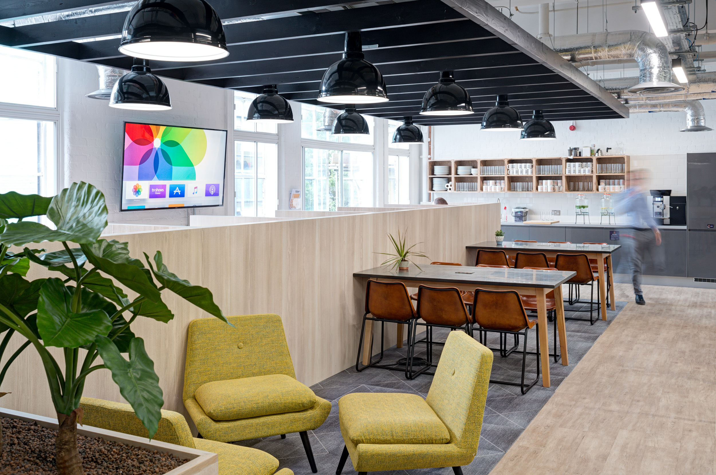 Worklife Clerkenwell teapoint seating area designed by Modus Workspace, combining casual seating and worktables under sleek black overhead lights, perfect for networking and casual work sessions.