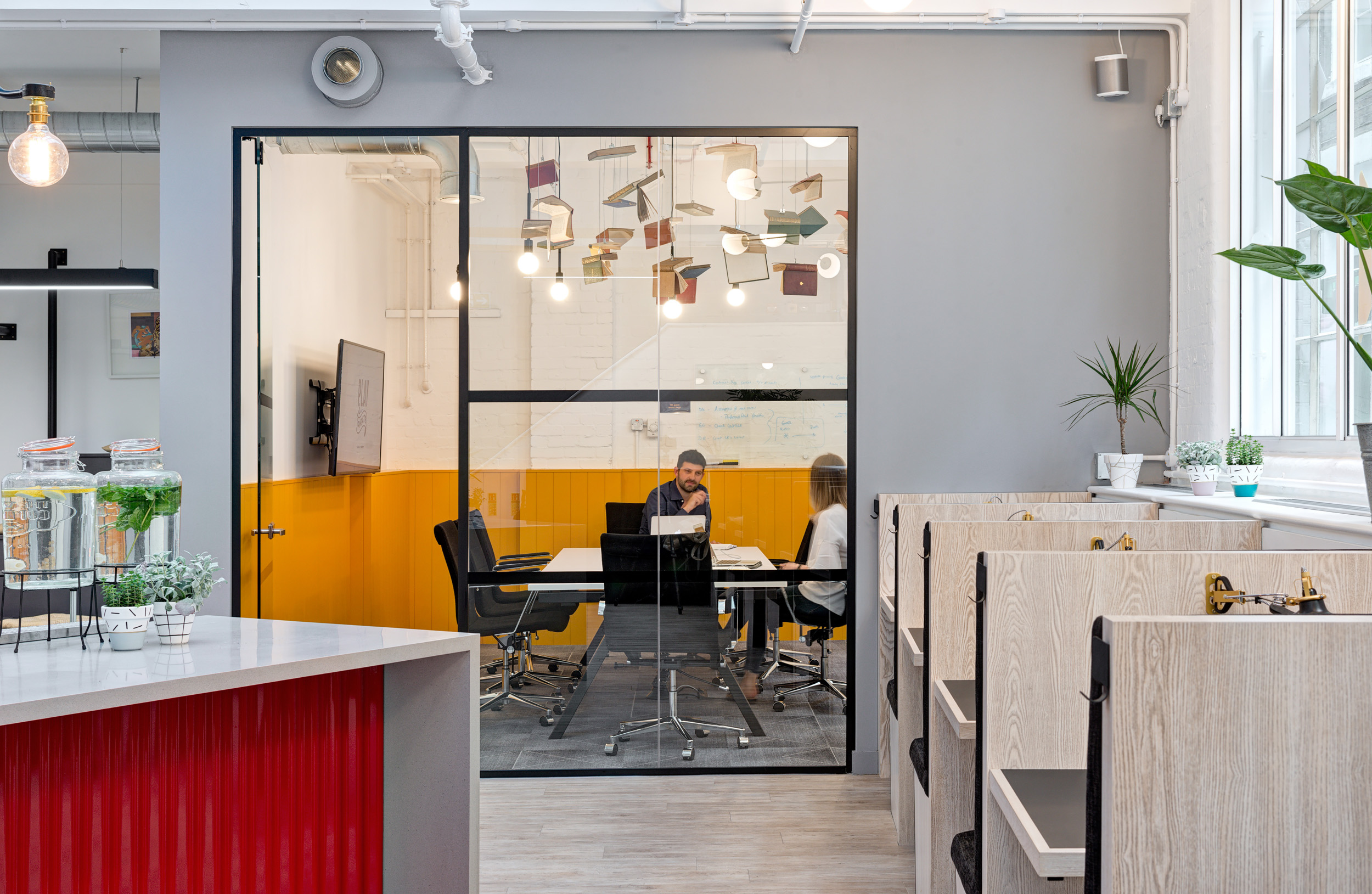Worklife Clerkenwell meeting room designed by Modus Workspace, with glass walls, contemporary lighting, and a quirky ceiling decoration of hanging books, ideal for creative brainstorming sessions.